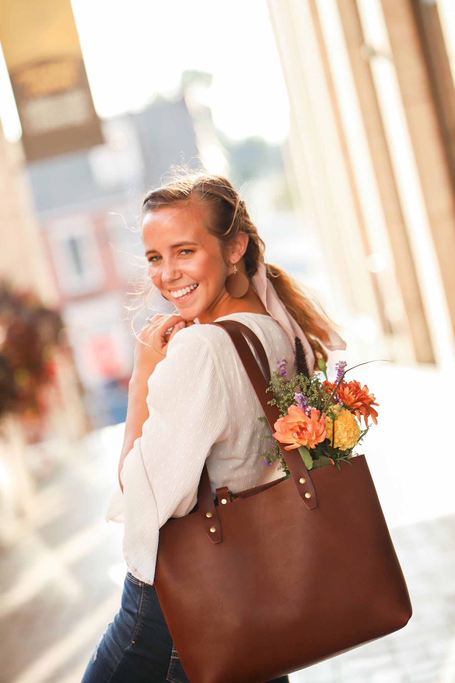 Our Leather Everyday Earrings pair perfectly with your favorite Urban Southern handcrafted leather bag. Shown is a woman wearing the Leather Circle Everyday Earrings in Chestnut Brown while carrying the Urban Tote in Chestnut Brown.