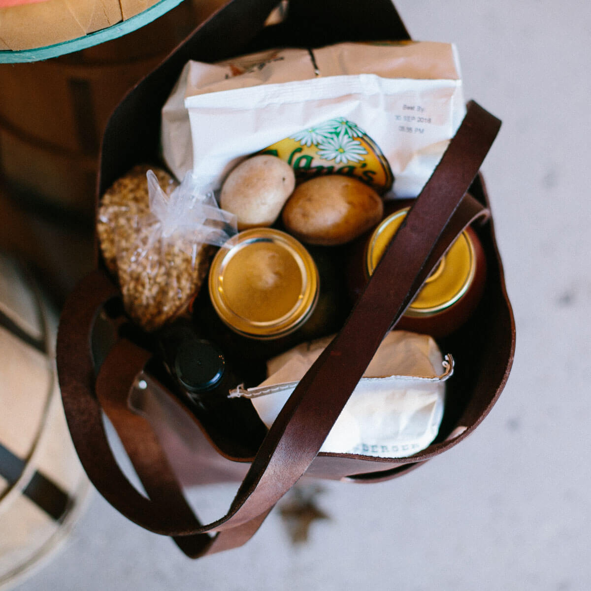 The Urban Southern Market Tote is shown with vegetables, jars, and bags of food inside.