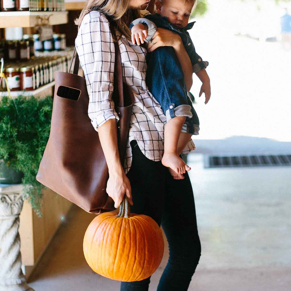 A woman carries the Market Tote on her shoulder while carrying a child and a pumpkin.