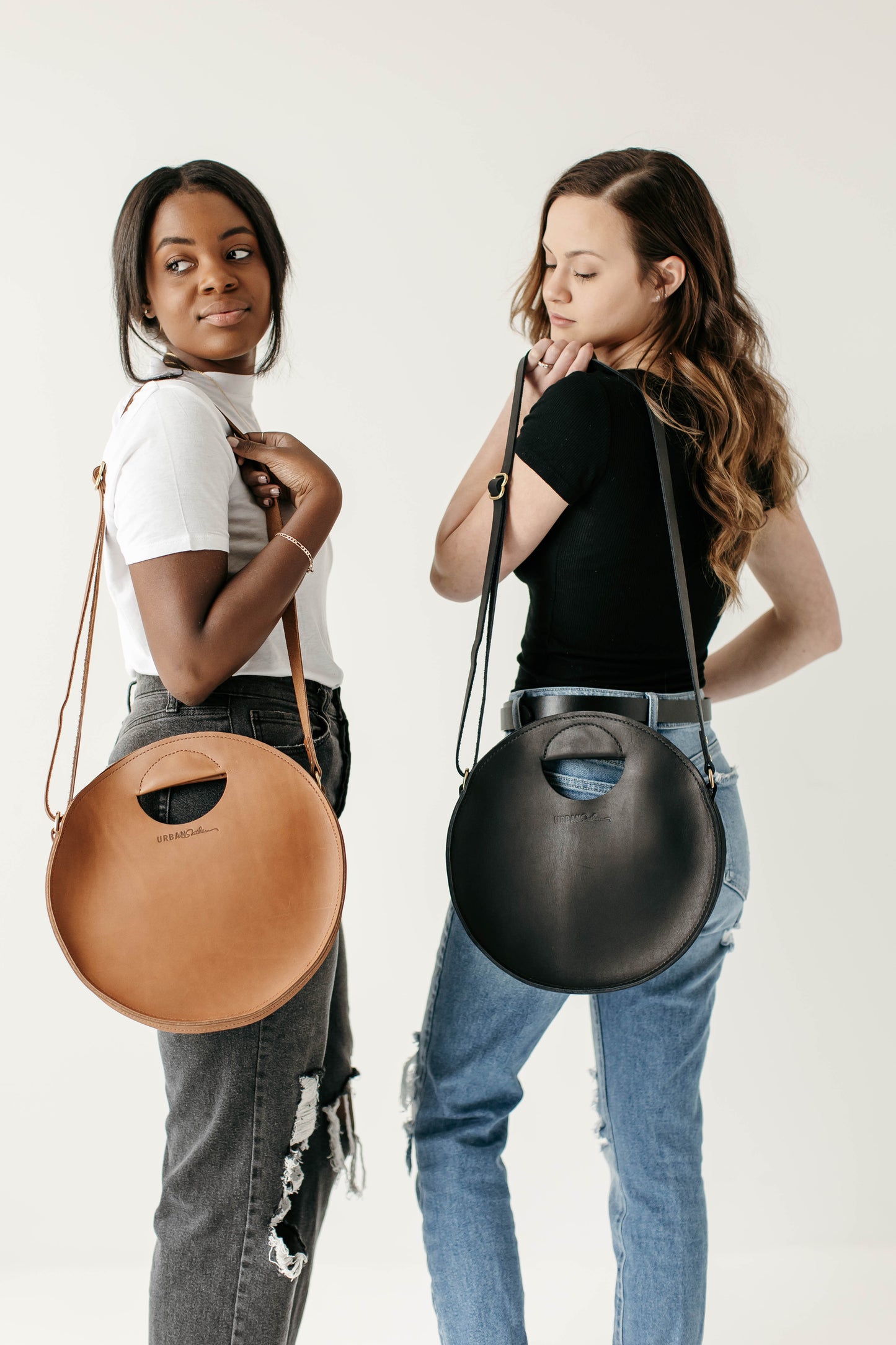Two women carry the Britt Circle Crossbody over their shoulders, one in Black and one in Honey.