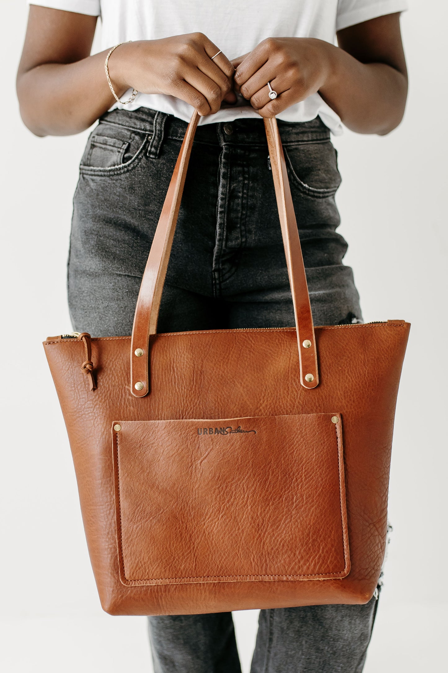 A woman holds a cognac leather Zipper Tote by its bridle leather handles.