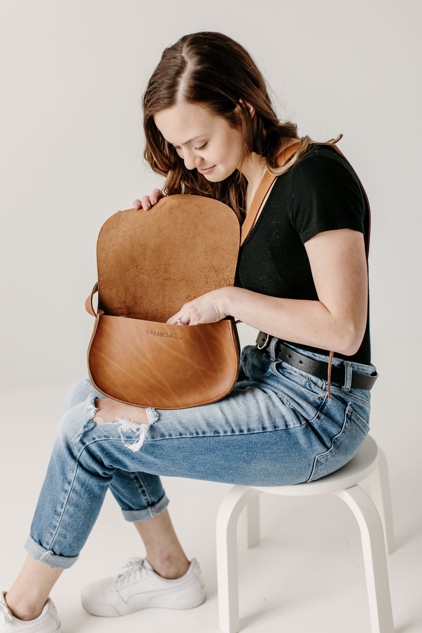 A woman holds the flap open to search inside her Urban Southern Half Moon Crossbody bag in Honey.