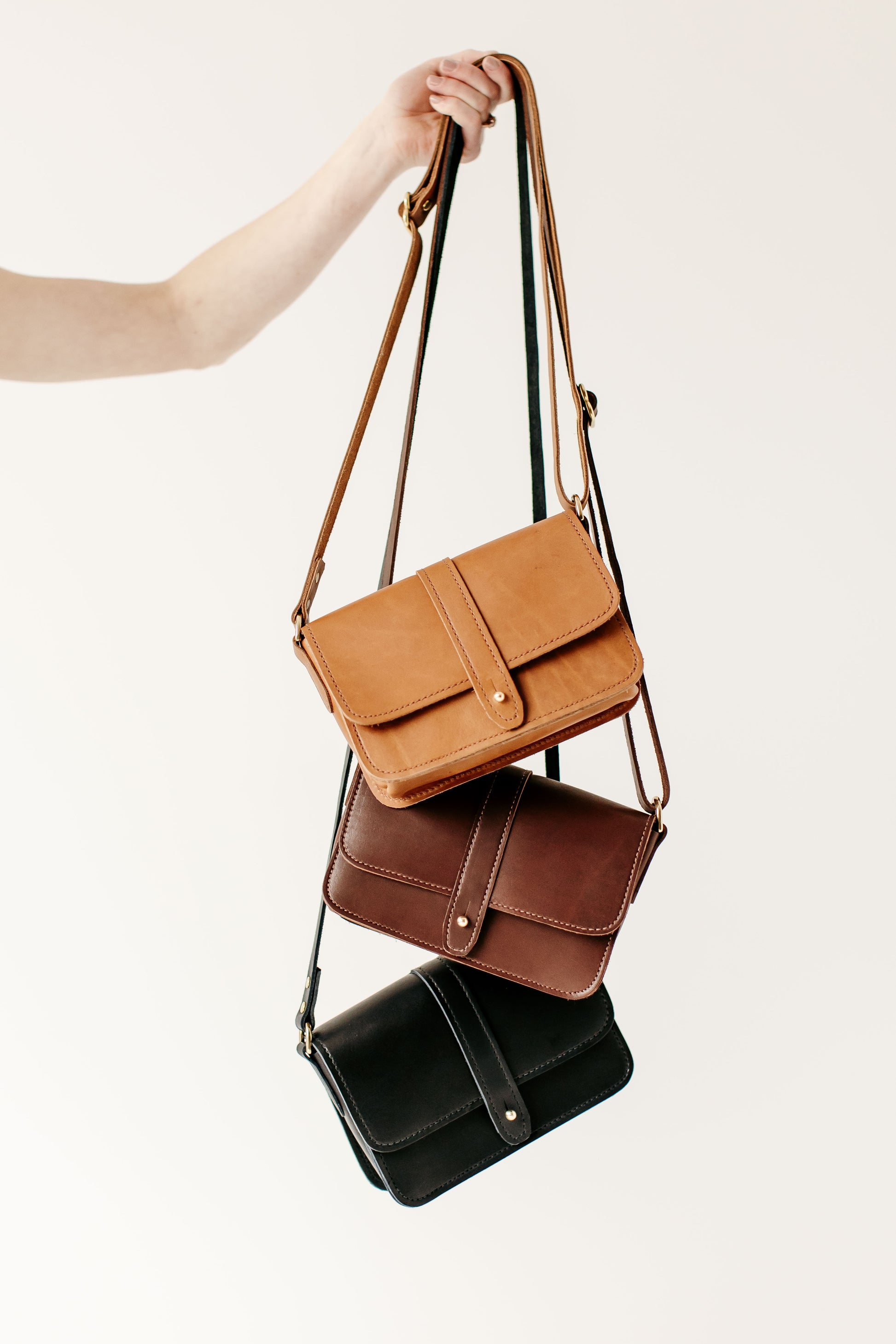The Urban Southern handcrafted leather Lancaster 5-Pocket Crossbody bag is shown in three colors: Honey, Chestnut Brown, and Black.