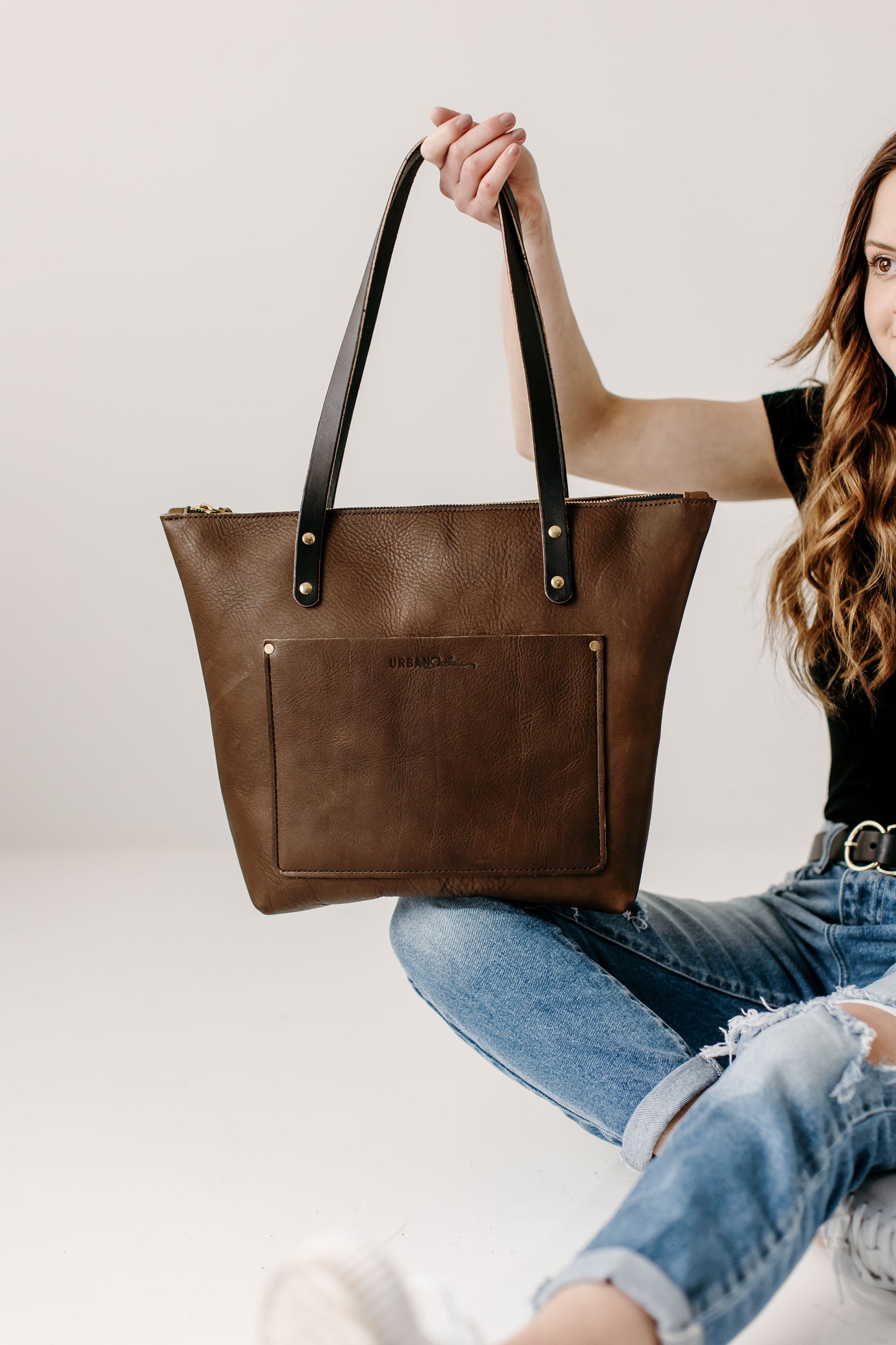 A woman holds a mocha Urban Zipper Tote by its contrasting leather handles.