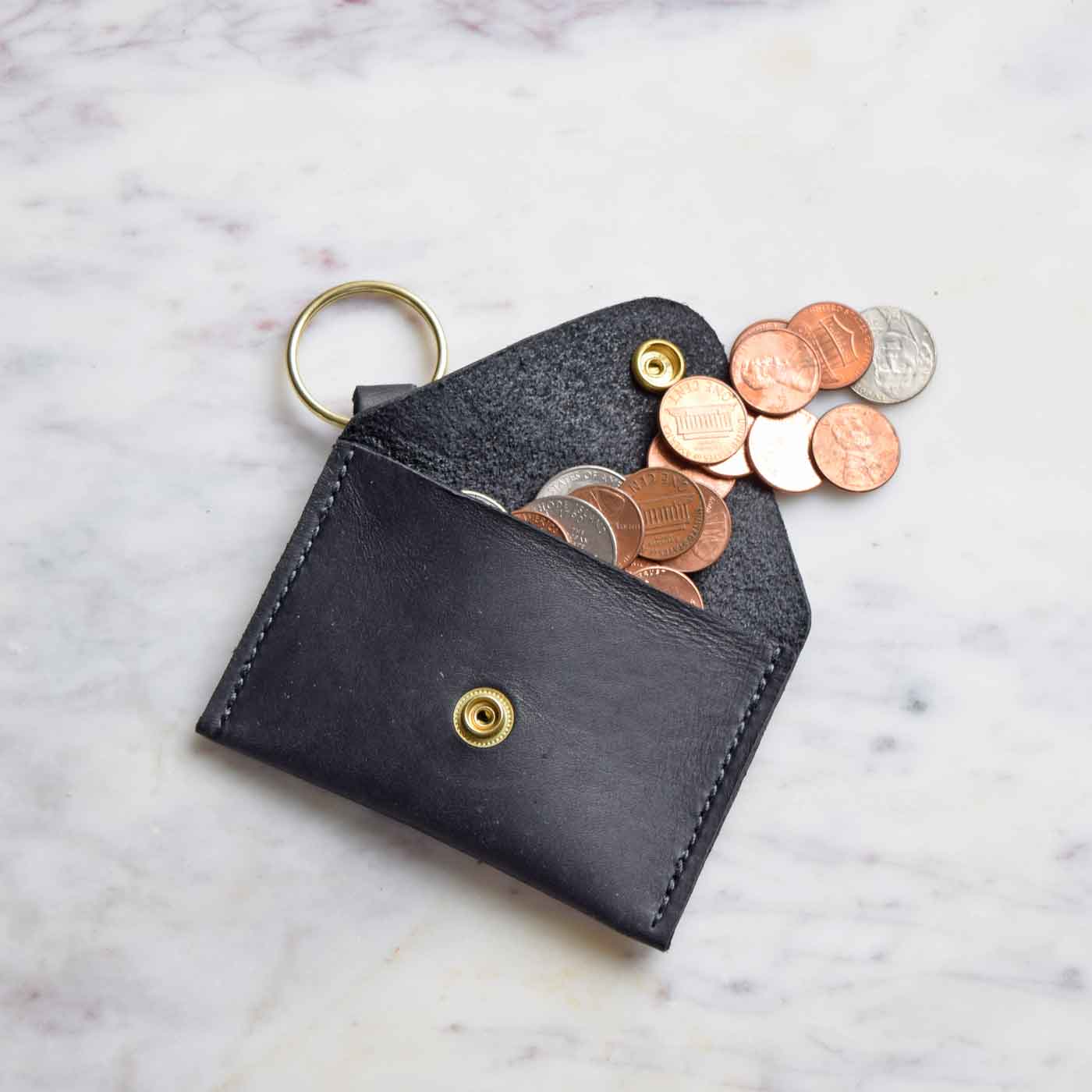 Coins pour out of the Keychain Coin Purse in Black.