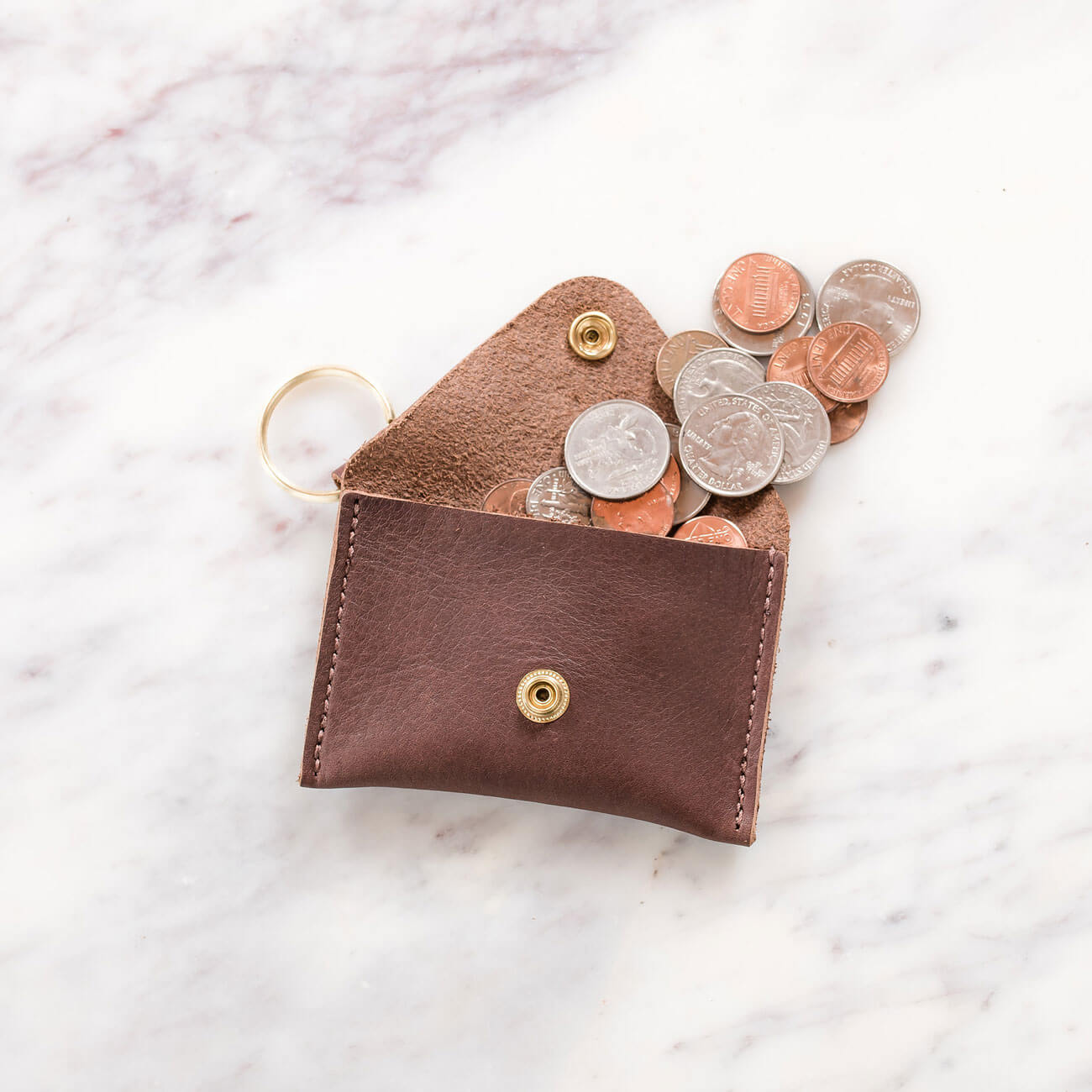 A pile of coins, including quarters, dimes, nickels, and pennies, pour out of the Urban Southern Keychain Coin Purse.