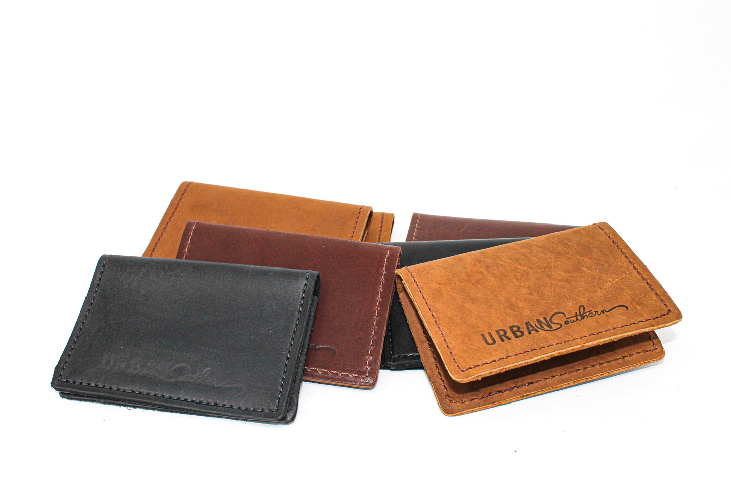 A pile of Handmade Leather Bifold Card Wallets in the different colors available: Black, Honey, Rustic Brown, and Chestnut Brown
