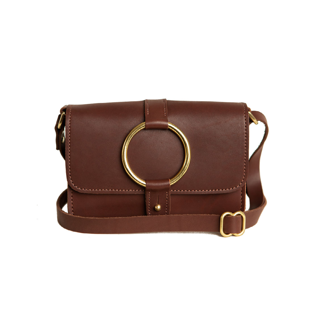 The Urban Southern handcrafted leather 5-Pocket Crossbody Bag in Chestnut Brown color, with handmade stitching, brass ring accent, brass post clasp, adjustable leather strap, and engraved Urban Southern logo.