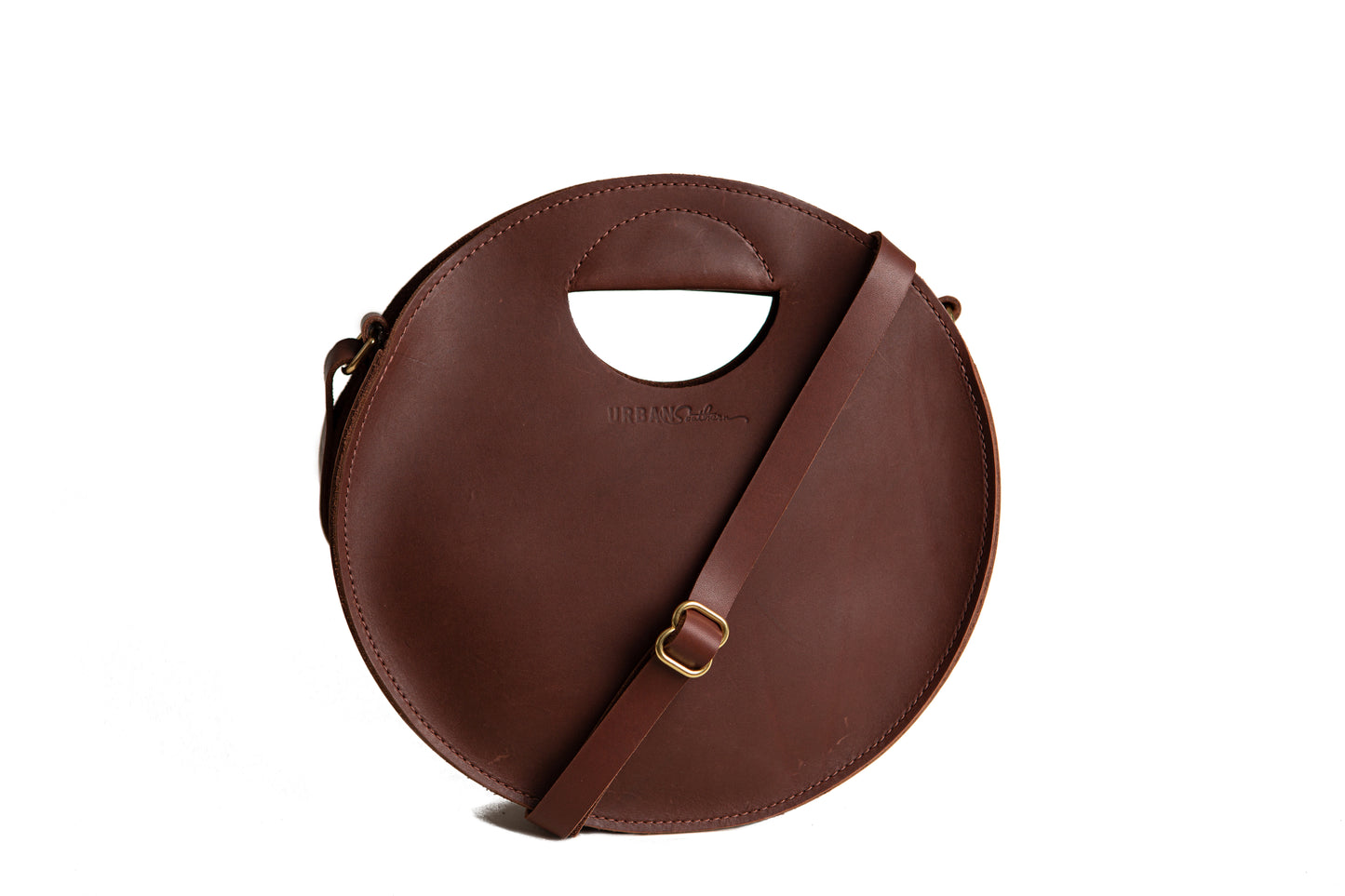 The handcrafted leather Britt Circle Crossbody Bag with adjustable strap and engraved Urban Southern logo, in Chestnut Brown.