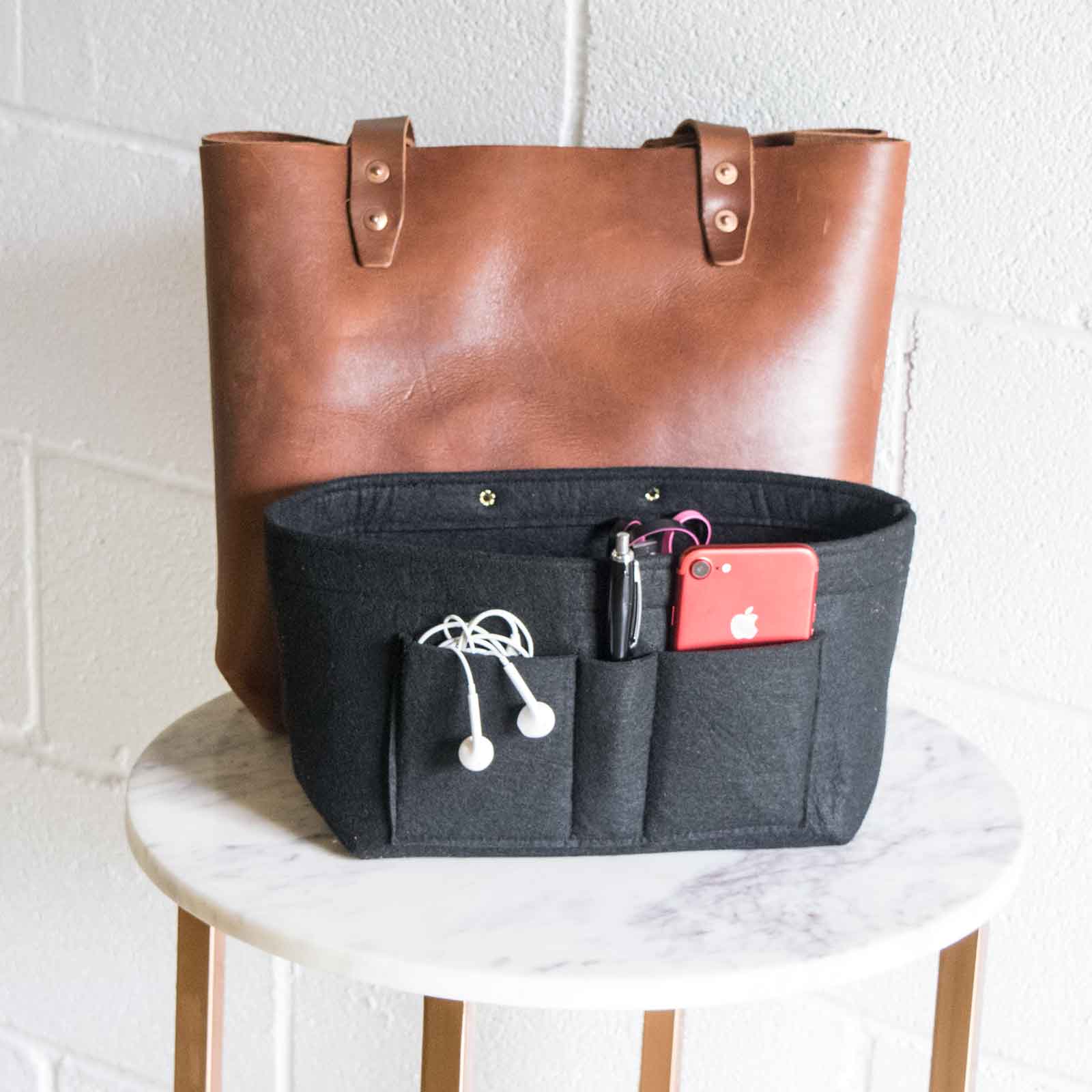 The tote insert pockets are shown with earbuds, a cell phone, pen, and other items.