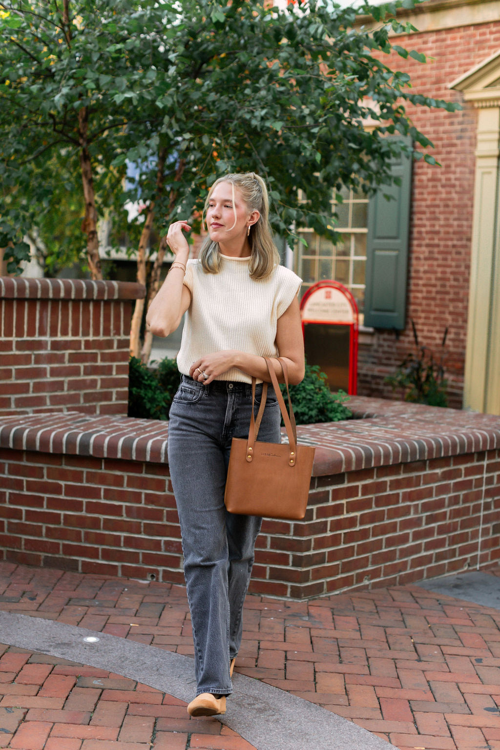 A woman walking down the street, carries a honey Mini Urban Tote on her arm. 