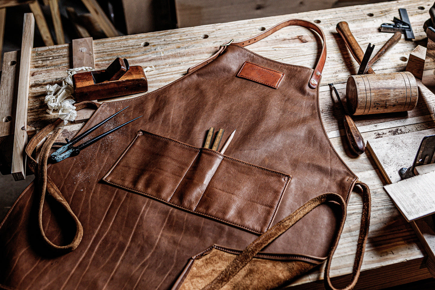 Brown leather apron on a wooden workbench with tools