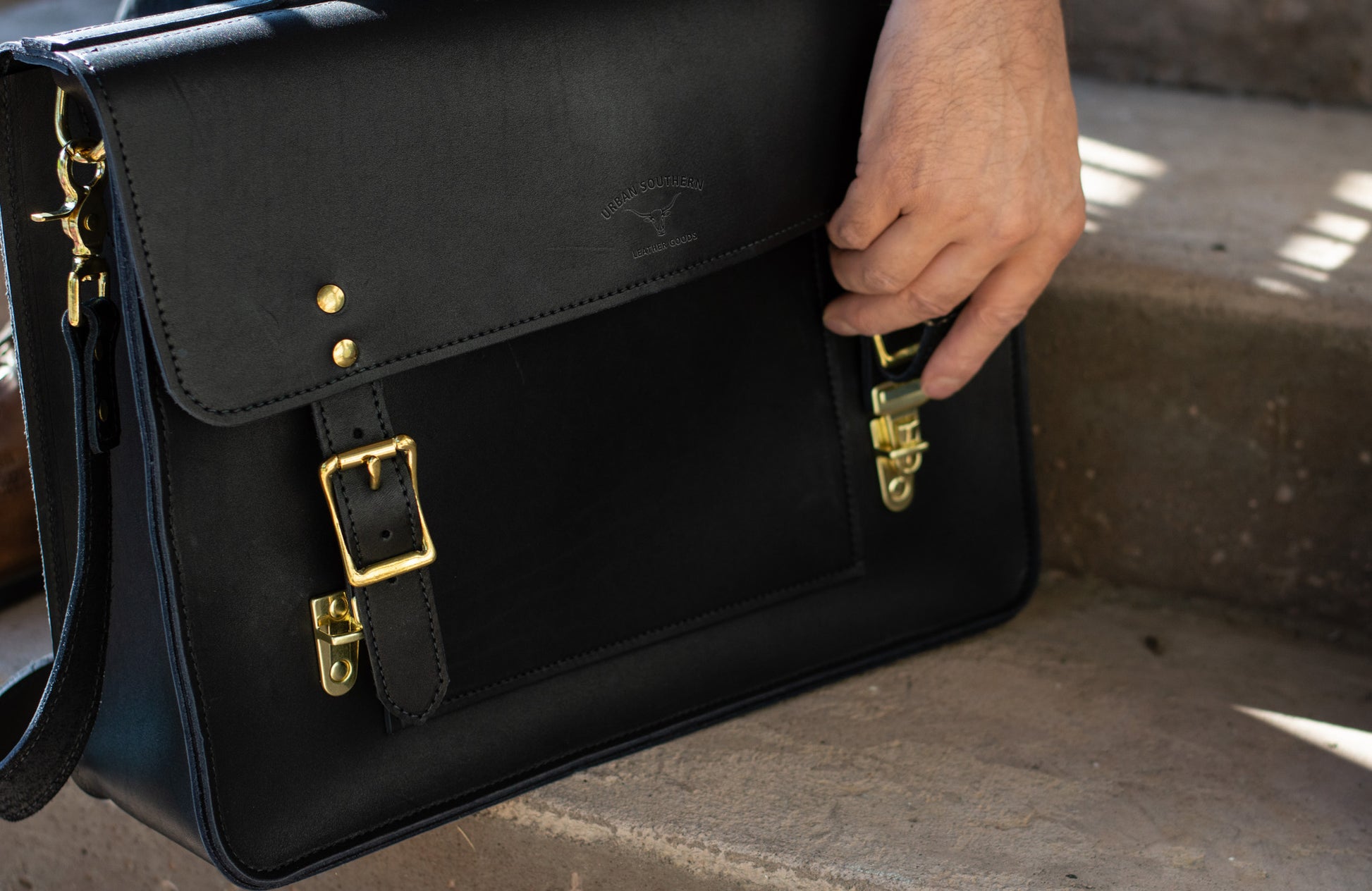 A man showcases the convenient hidden quick-release clasps of a black Executive Briefcase. 