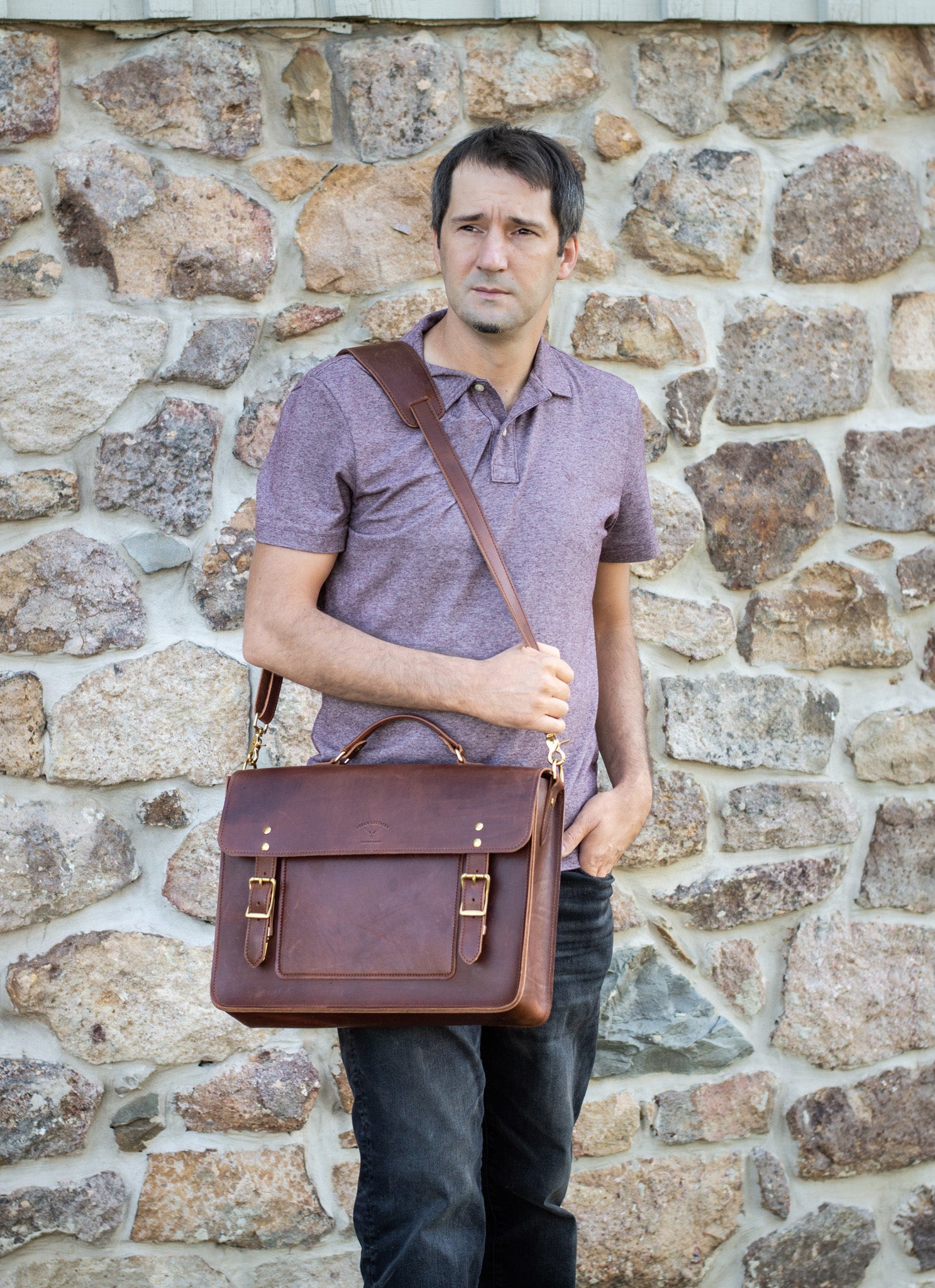 A man holds an Executive Briefcase in the whiskey leather color, on his shoulder. 