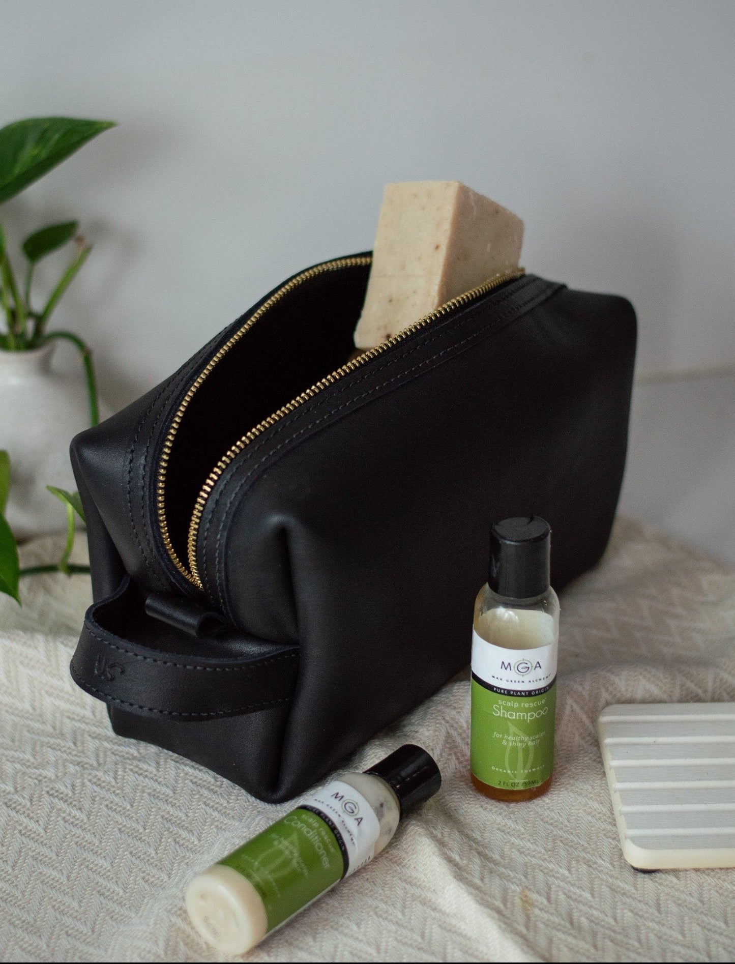 Black leather dopp kit sitting on a counter, with the zipper open showing a bar of soap.