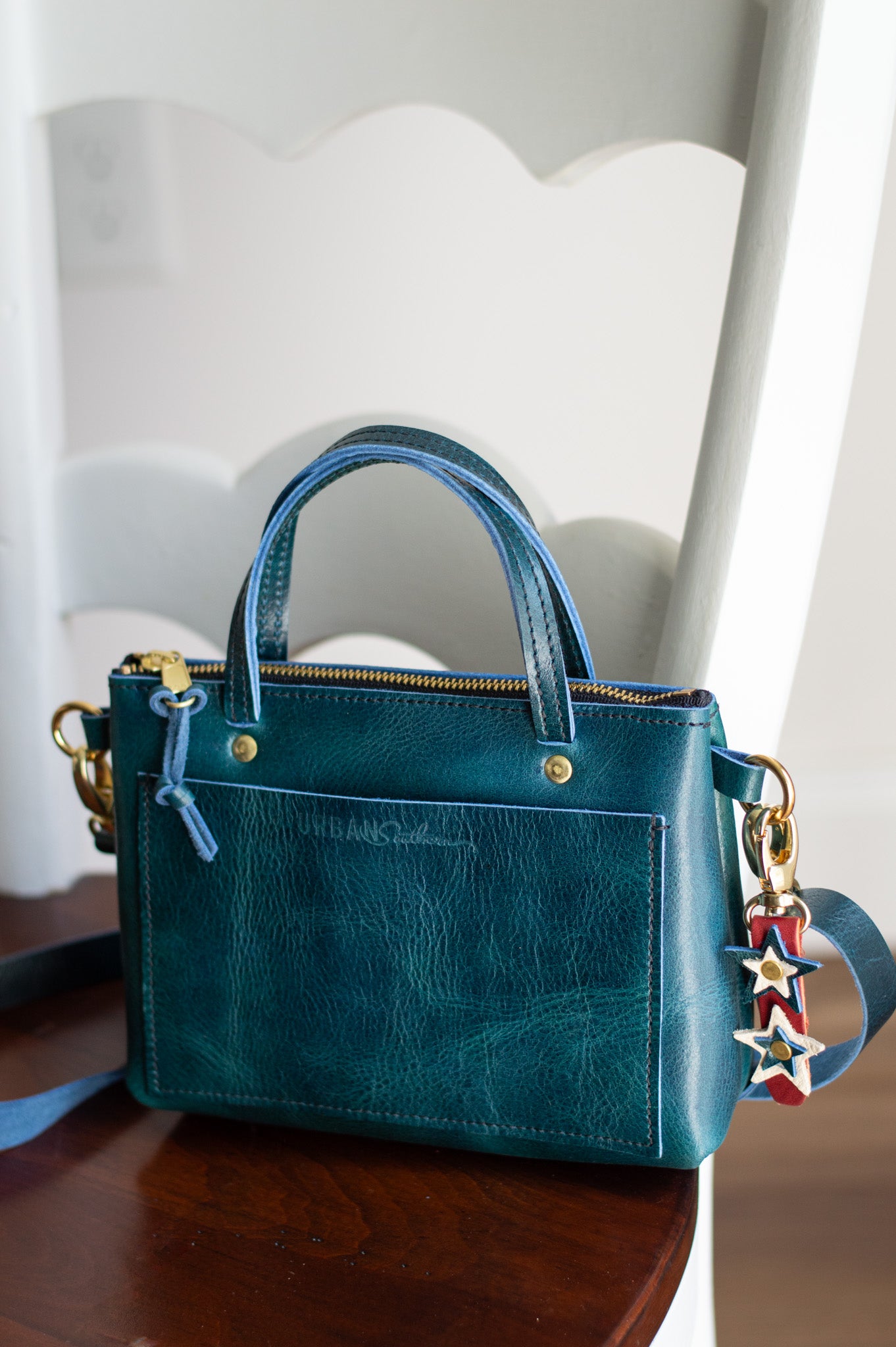 Teal handbag with a colorful jubilee bag charm clipped to the side ring on a wooden surface