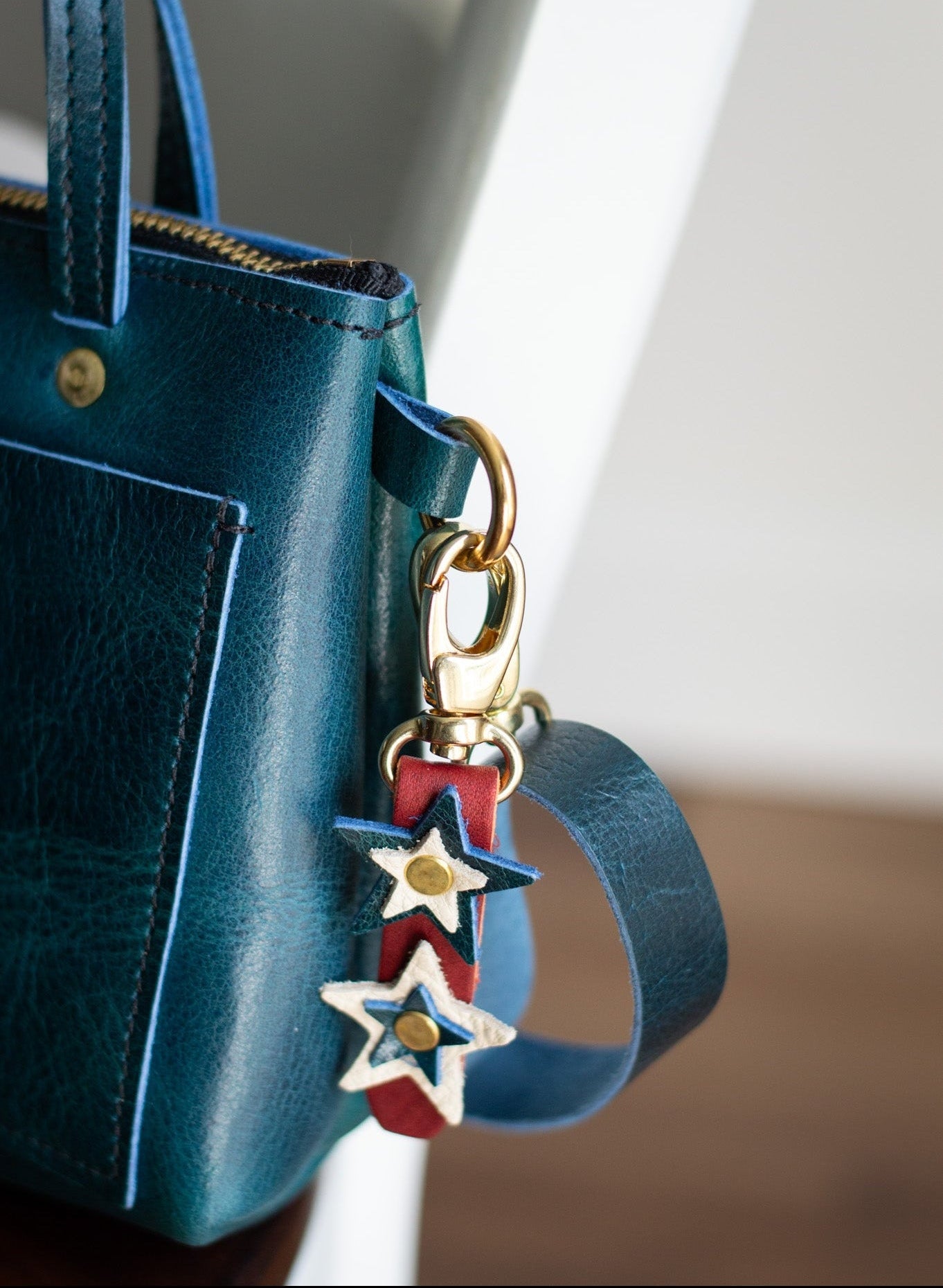 Blue handbag with a red, white & blue star-shaped keychain on a neutral background