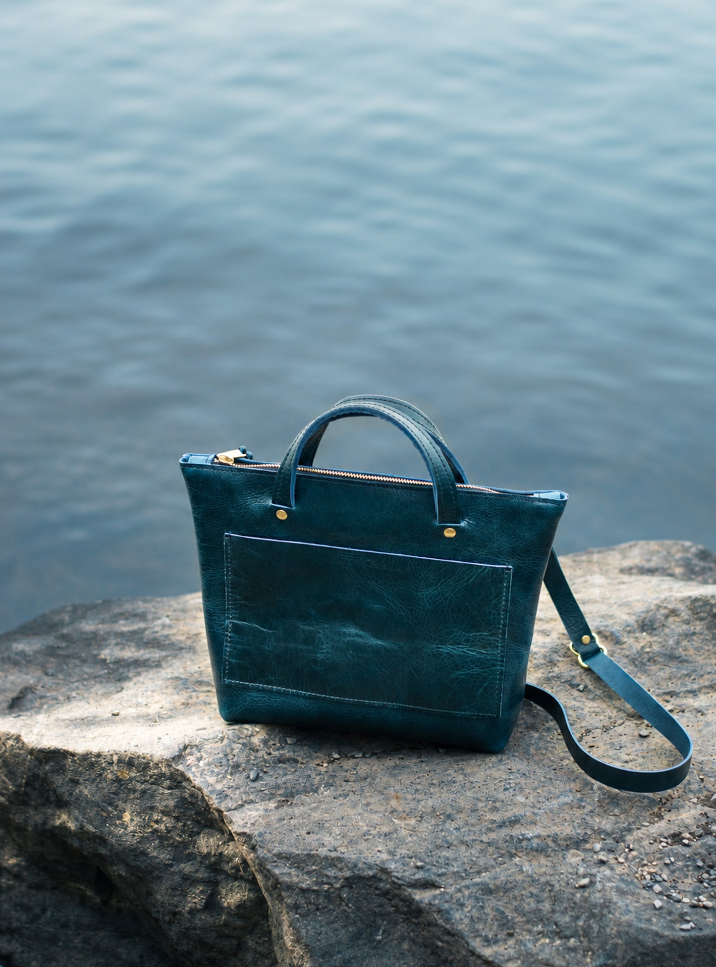 Teal blue leatehr cassidy crossbody on a rock with water in the background