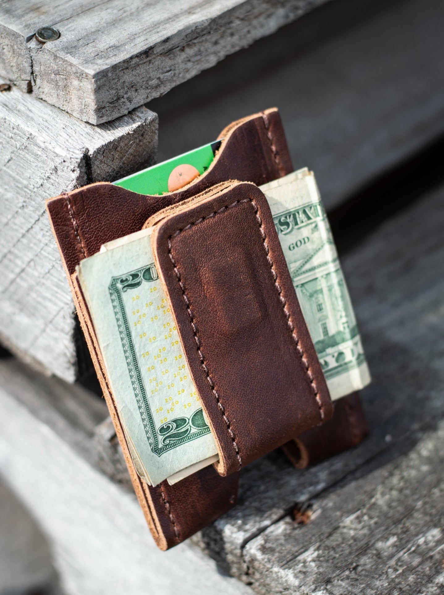 Brown leather wallet with money folded between the magnetic clip on a wooden surface