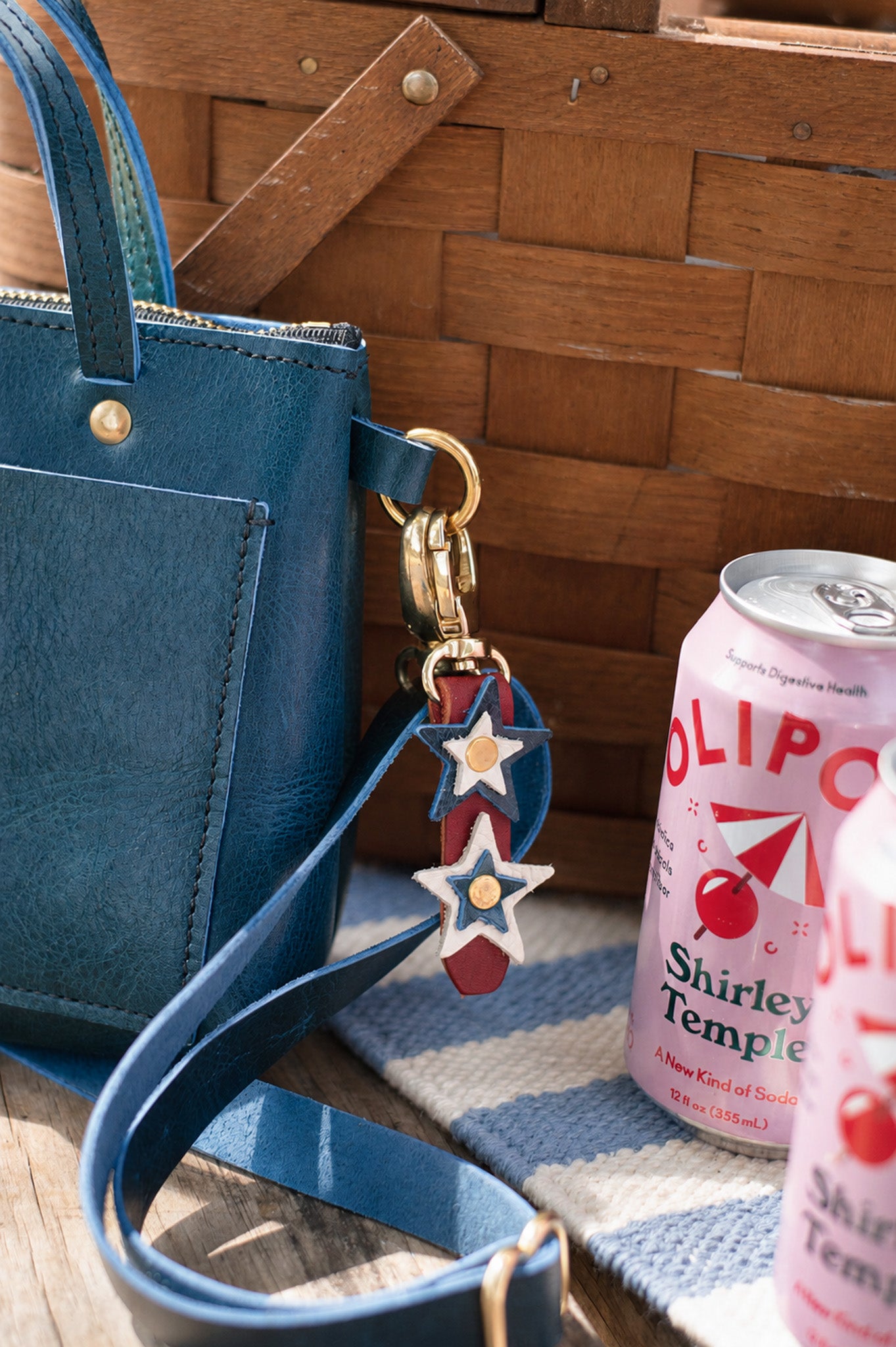 Blue handbag with a decorative red, white & blue star keychain and a can of soda on a wooden surface.