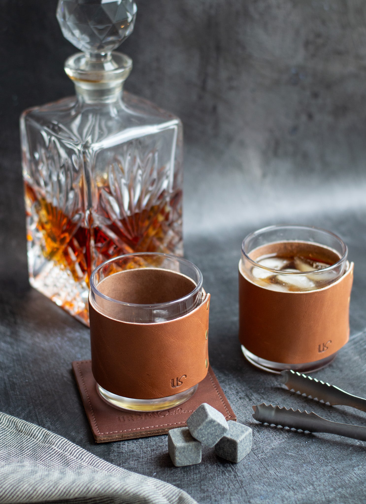 Two glasses with leather sleeves and a decanter on a dark surface.