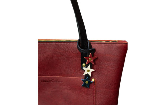 Red leather handbag with a red, white & blue star-shaped bag charm attached to the handle on a white background