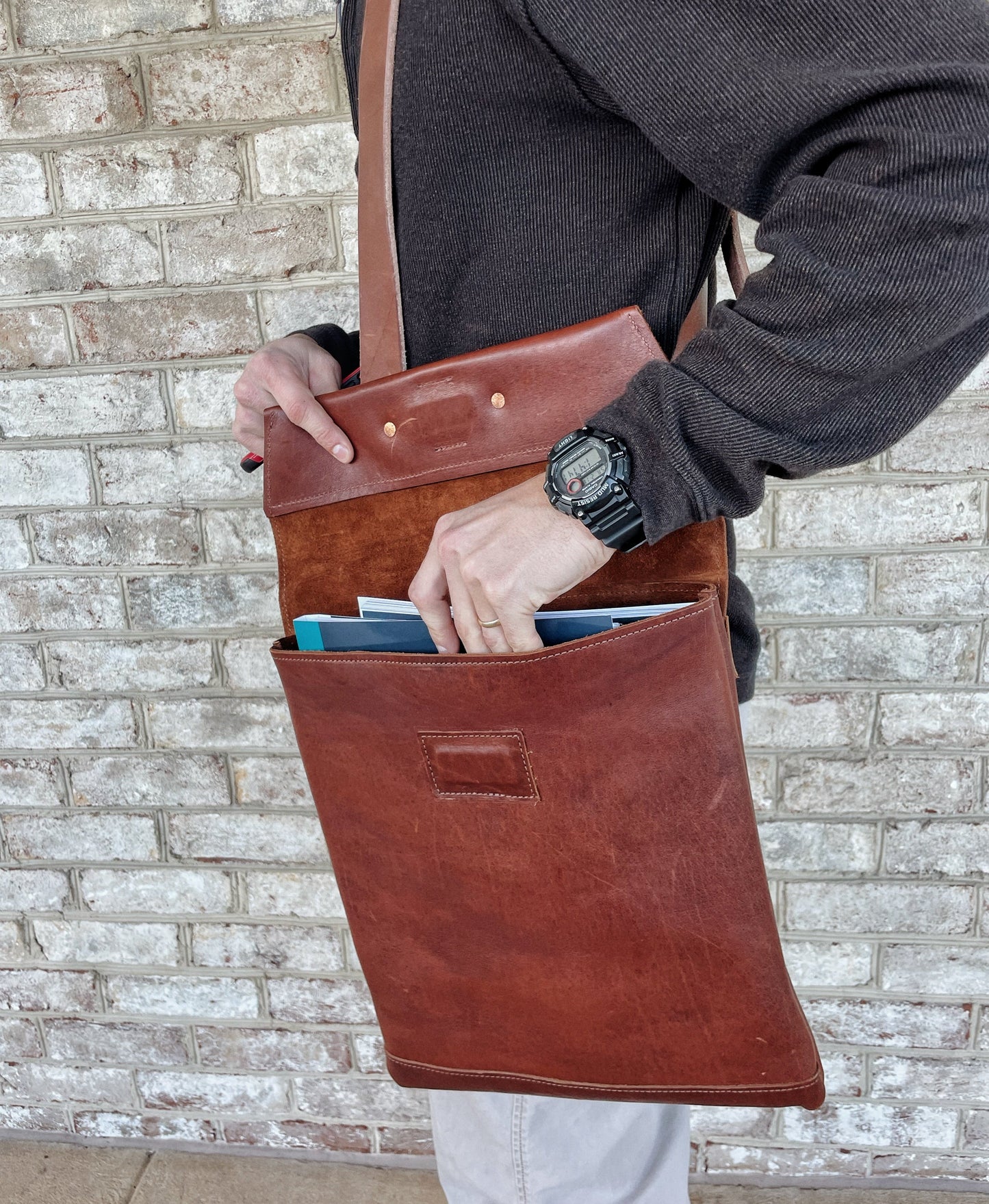 Man reaches into his brown leather satchel to remove a notebook. 