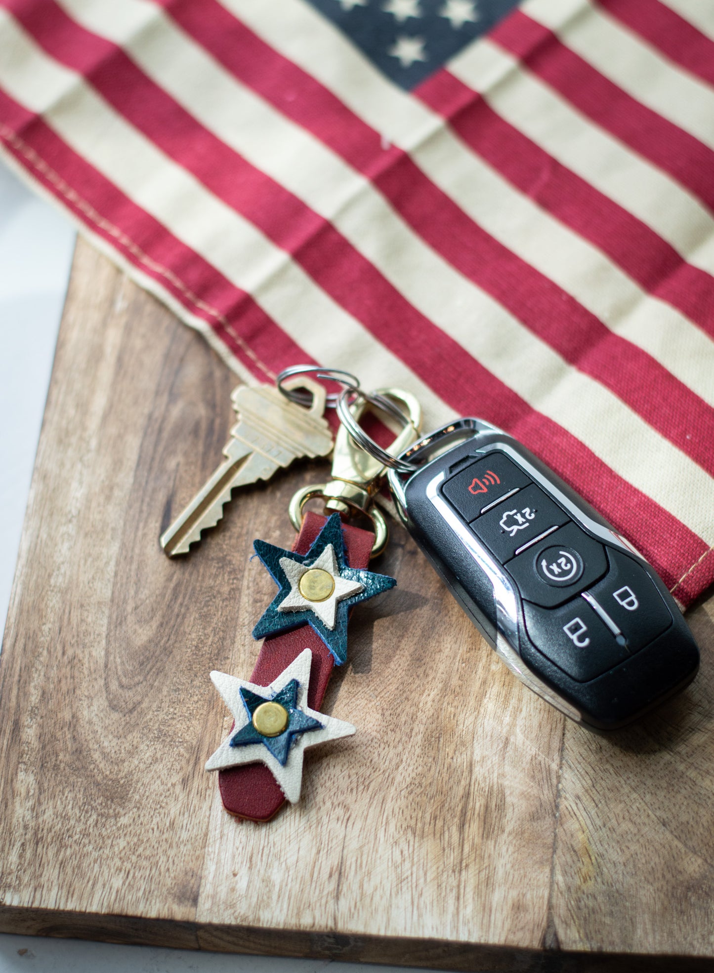 Keychain with red, white & blue star charms on a keyring, placed on a wooden surface with an American flag in the background.