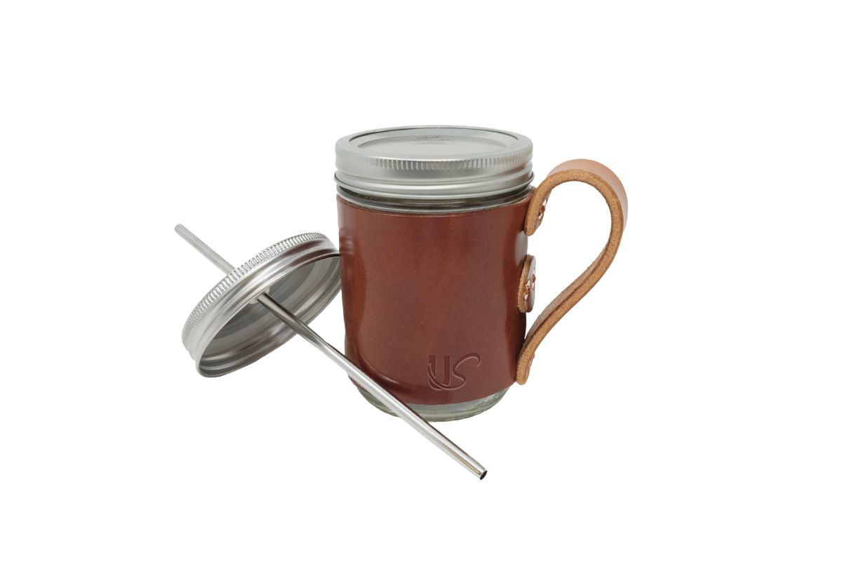 The Mason Jar Mug, featuring full-grain leather wrapped perfectly onto an glass mason jar, includes a lid with a metal straw. 
