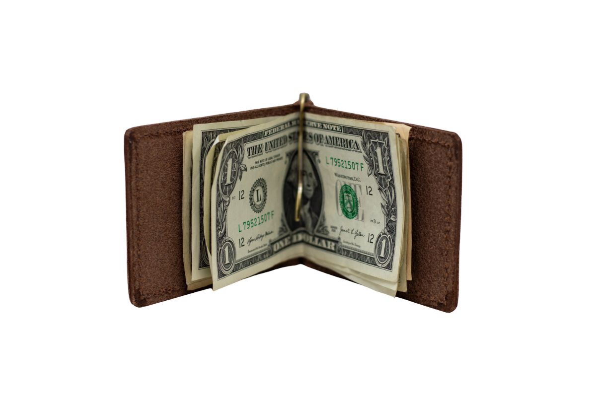 A brown money clip bifold wallet lies open with dollar bills clipped into the center brass money clip. 