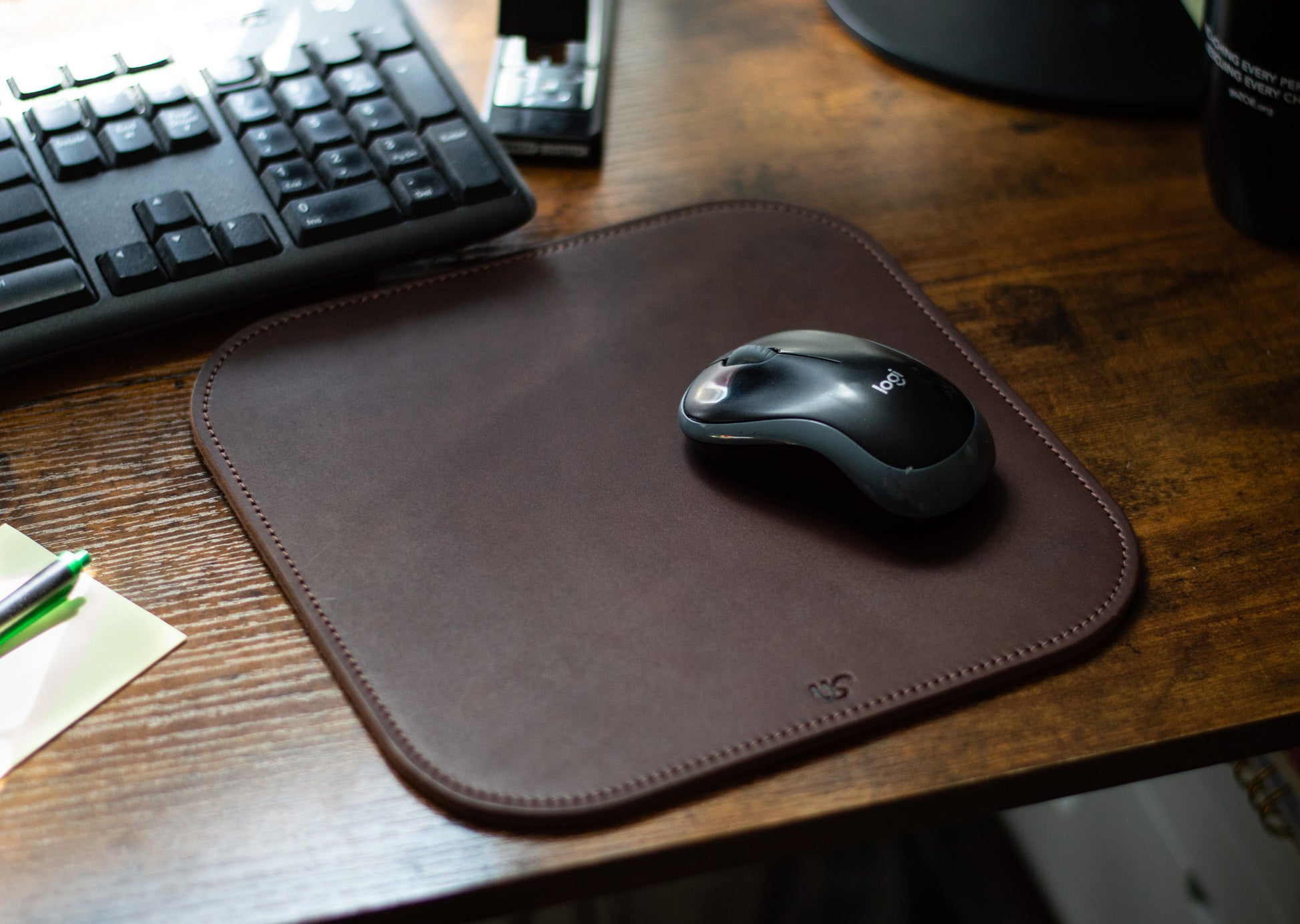 A computer mouse sits on top of a full-grain leather Mouse Pad that is laying on a desk in an office.