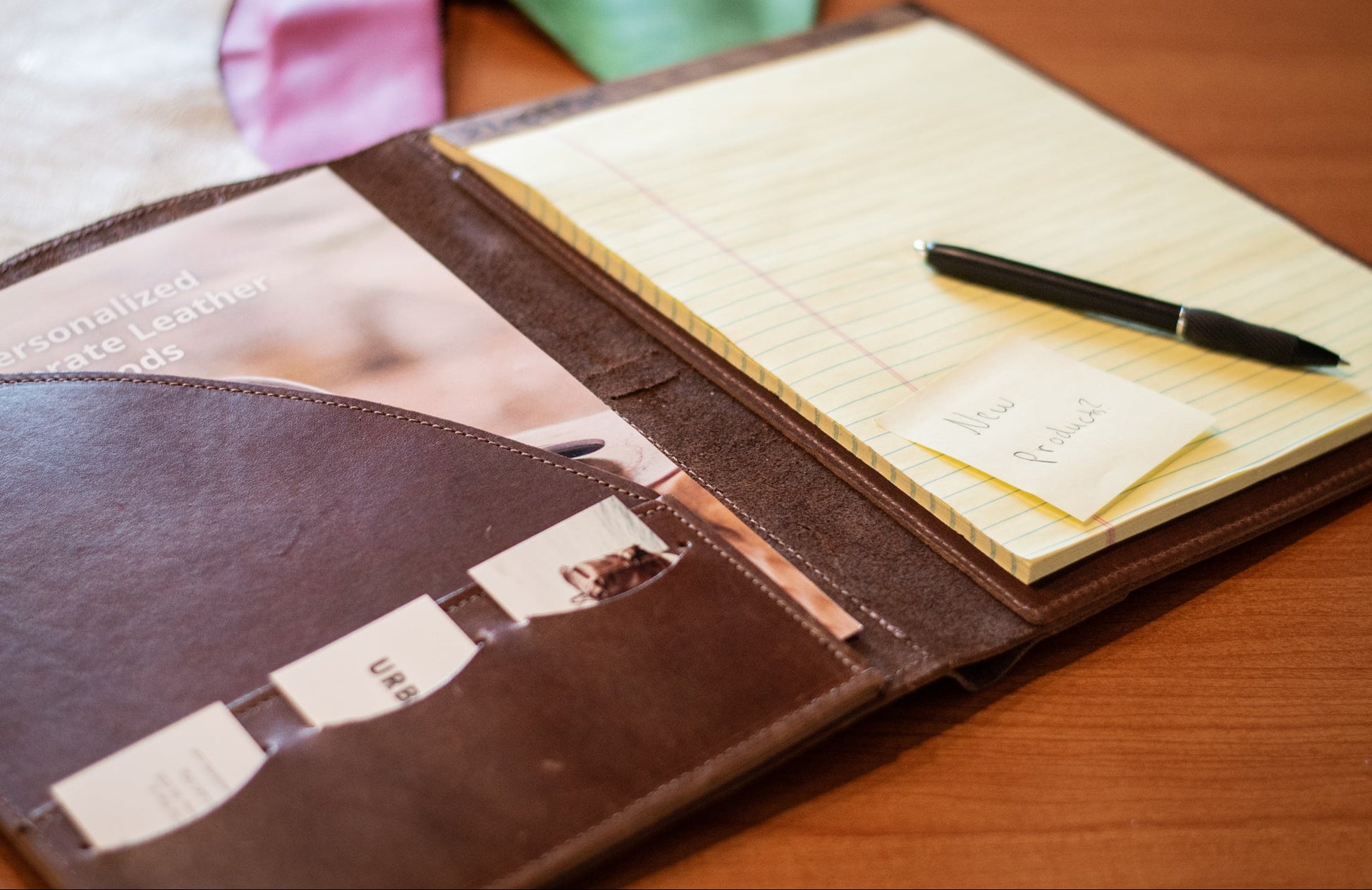 Brown leather padfolio with business cards in the card slots and a pen on a wooden surface.