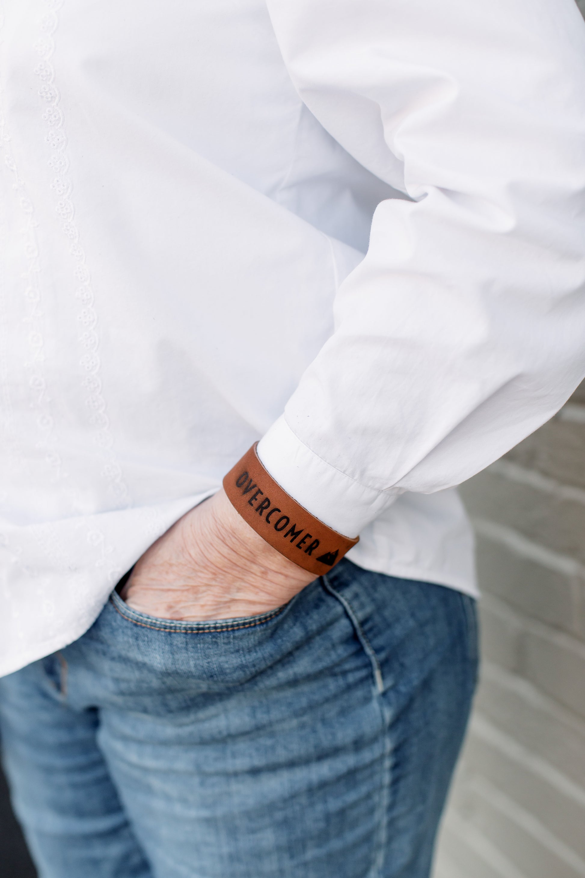 A person wears a leather 'Overcomer' Cuff on their wrist. 