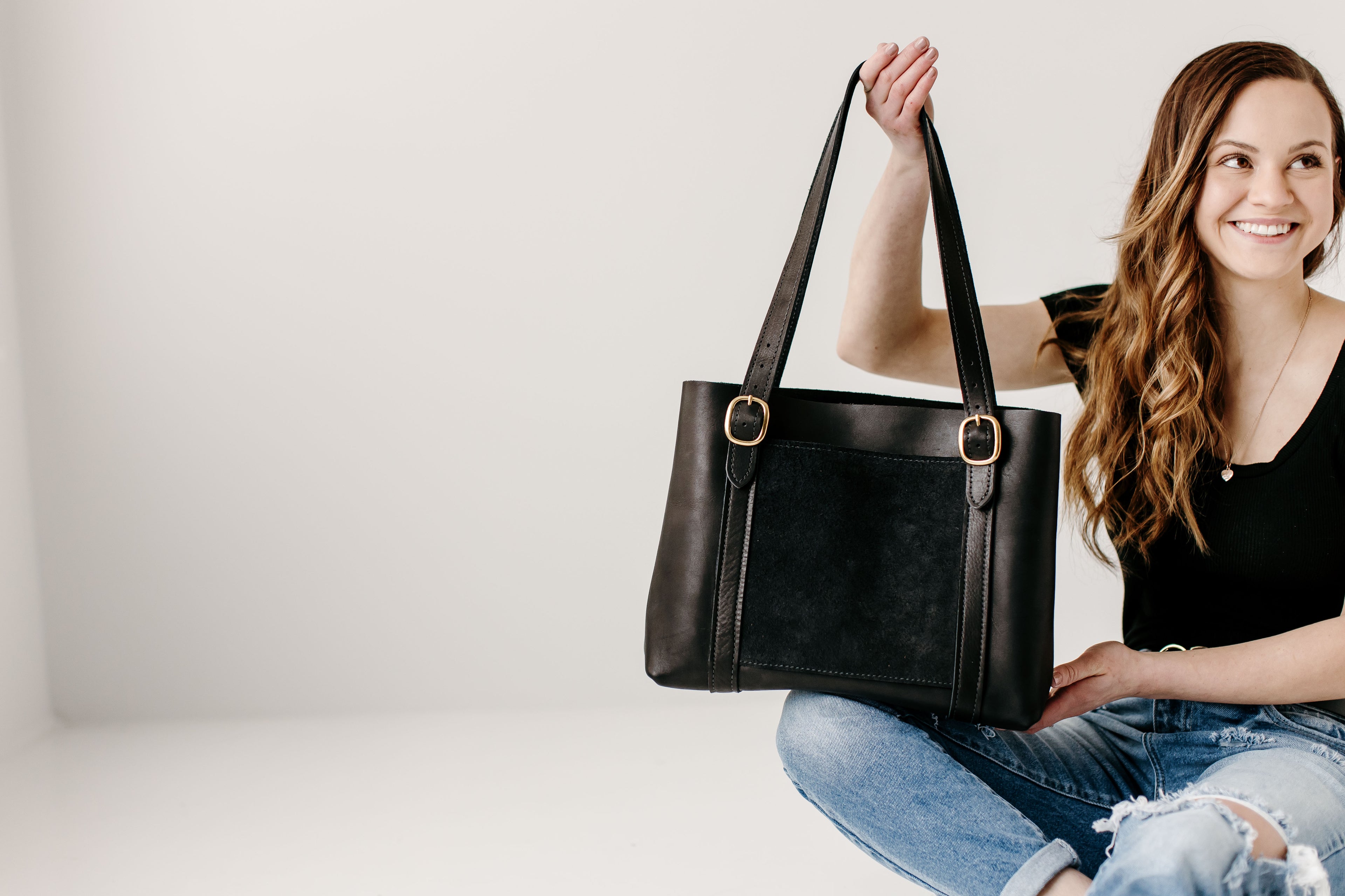 Woman holding a black leather handbag against a plain background