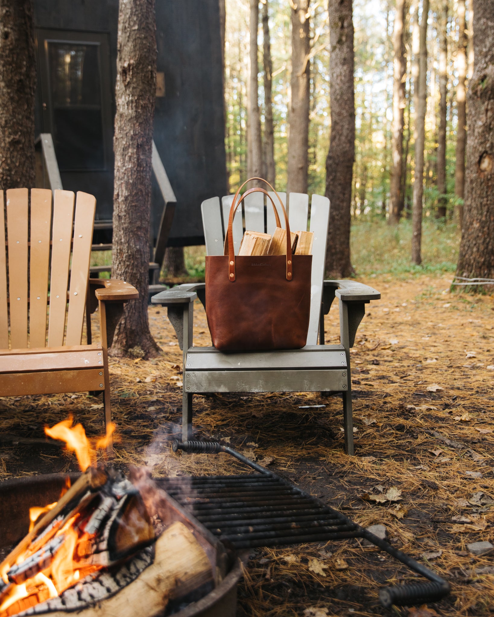 A brown leather handbag sits on an outdoor chair next to a fire pit.