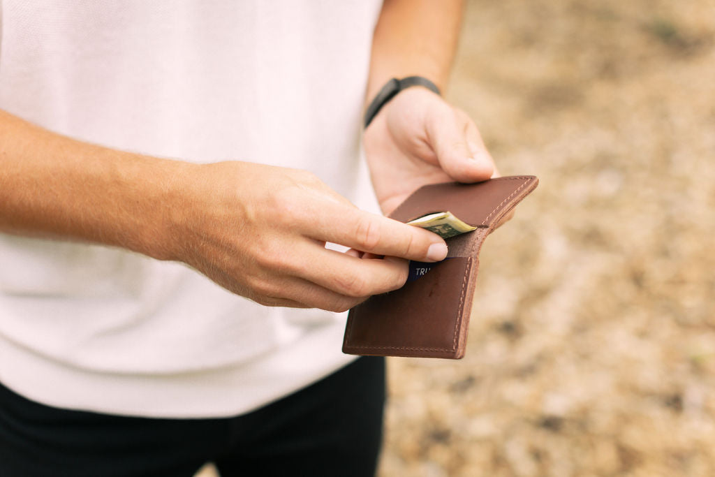 A man pulls dollar bills out of the interior pocket of a brown leather wallet