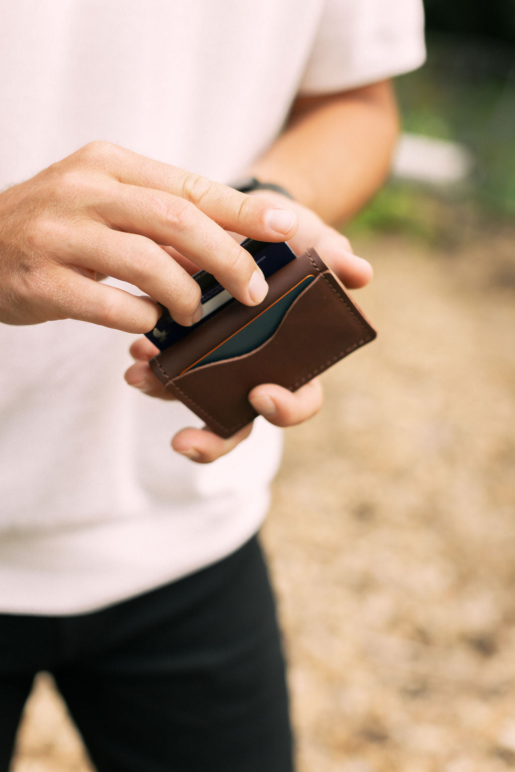 A man pulls a credit card out of an outside pocket of a brown leather wallet.