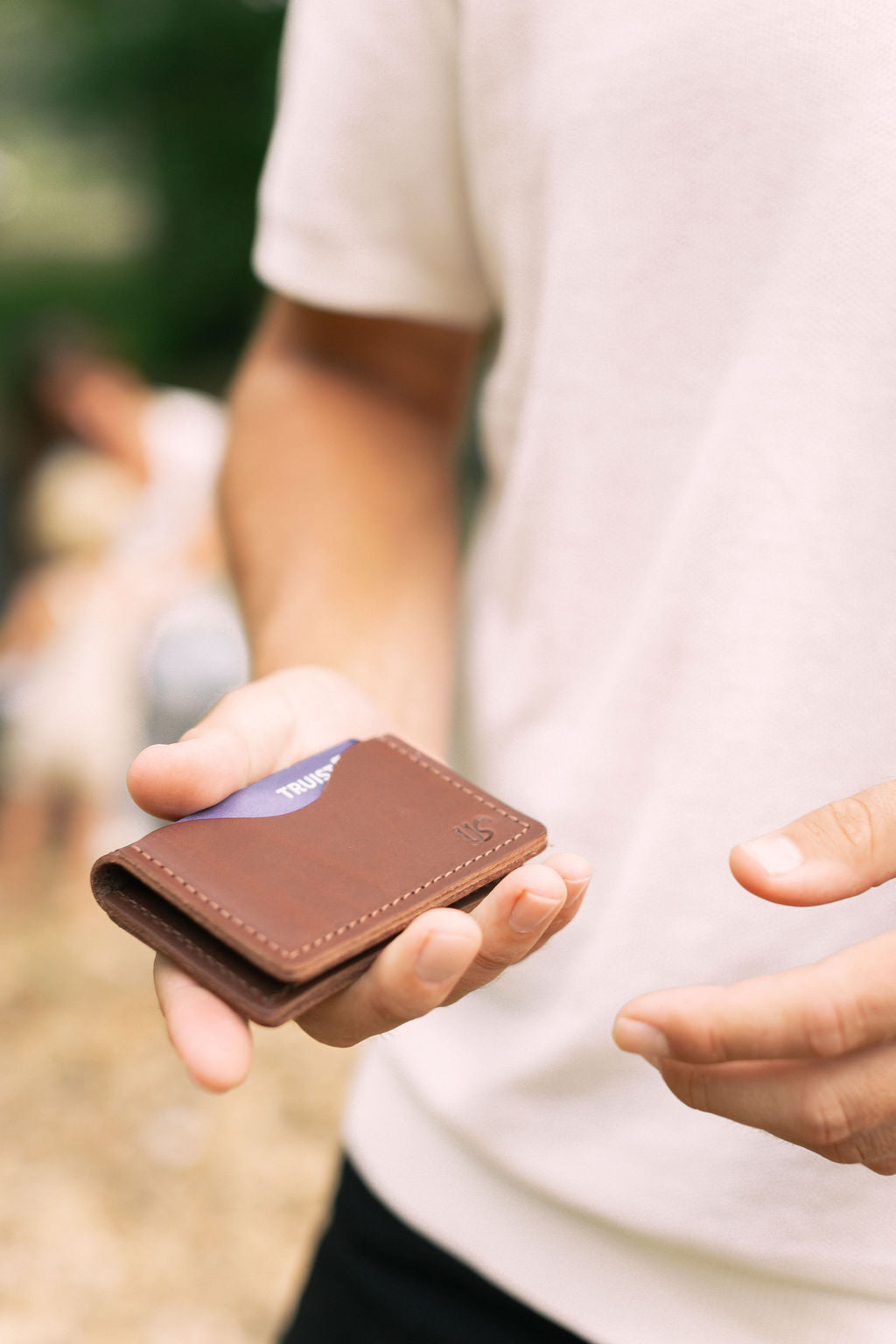 A man holds a brown leather bifold card wallet in his hand