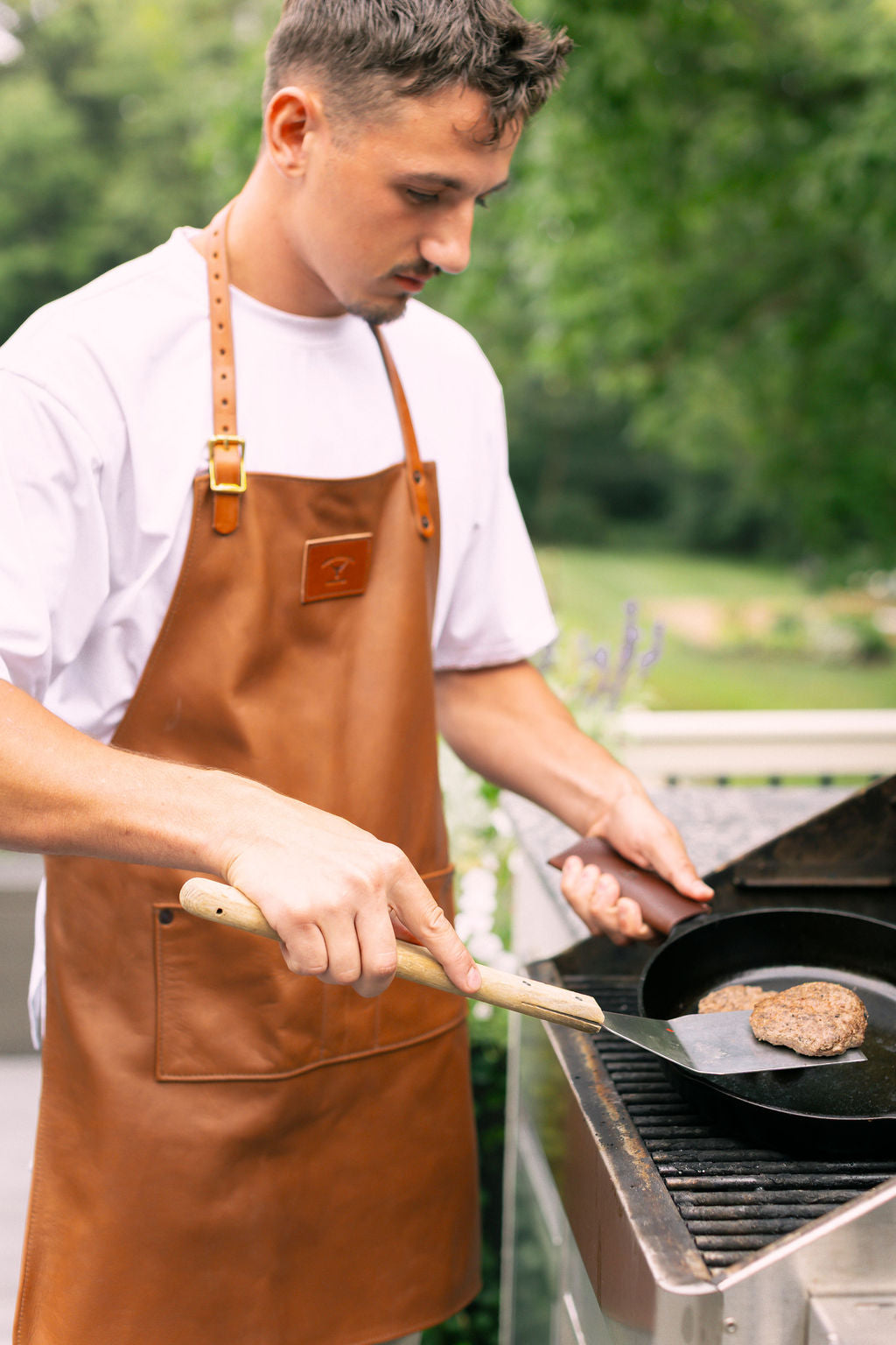Man grilling outdoors wearing a brown leather apron