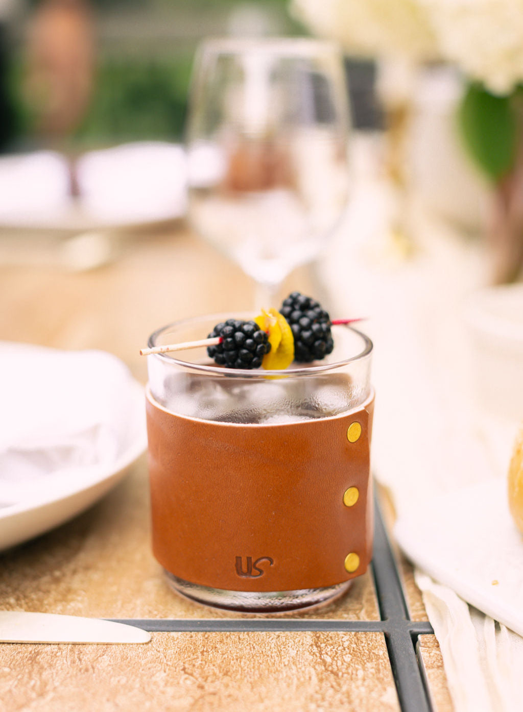 a leather wrapped whiskey glass sitting on a table garnished with a skewer of berries