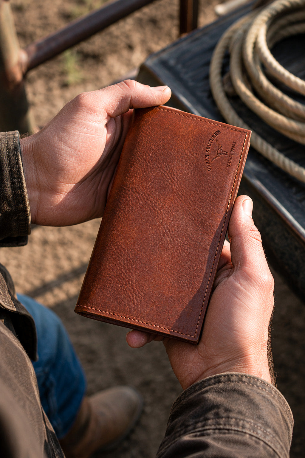 Brown leather wallet held by a man standing next to a truck bed.
