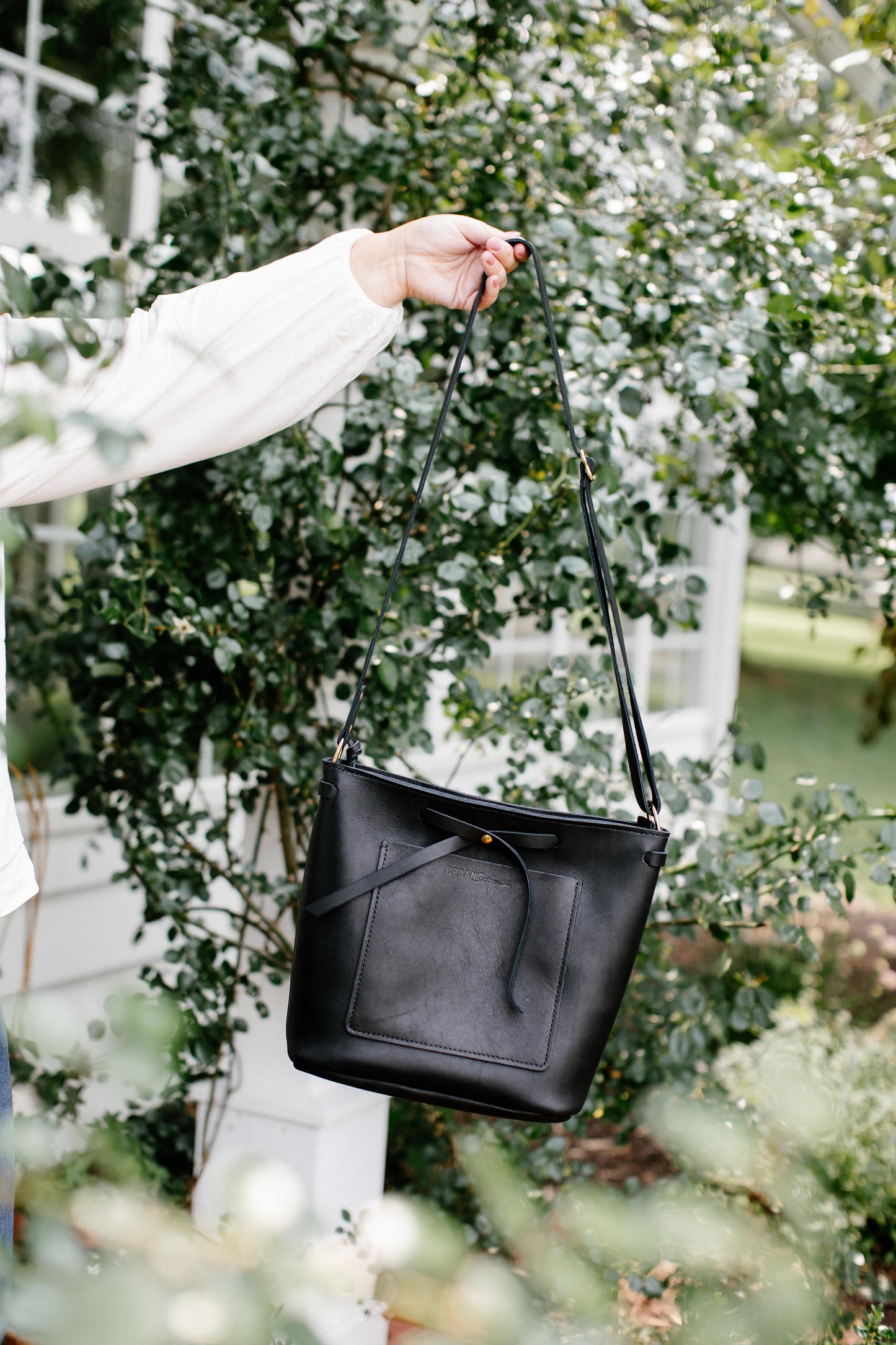 A woman holds a black Lexington Bow handbag by its adjustable shoulder strap, showcasing the spacious size of the bag.