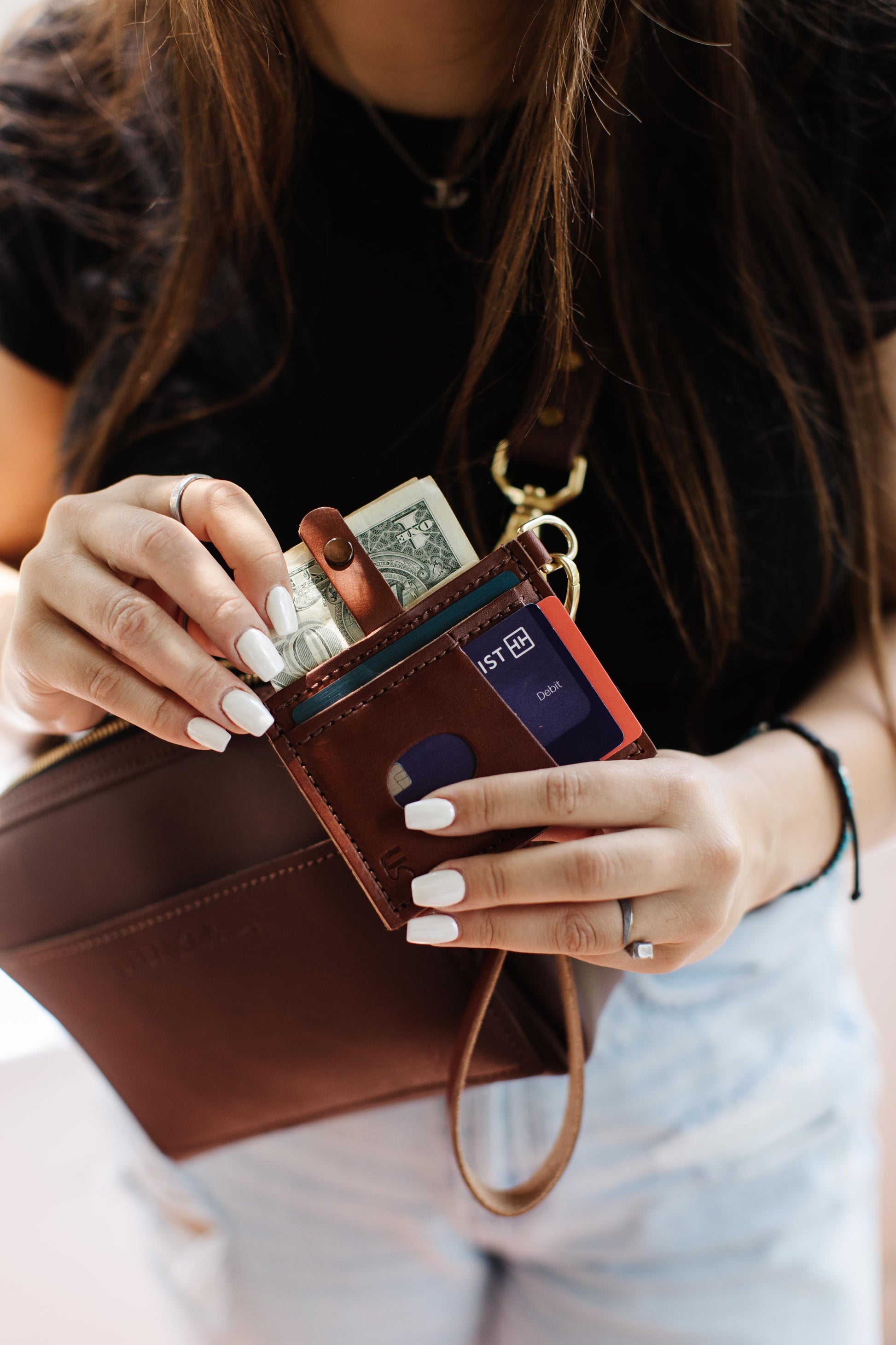 A woman pulls cash from her Urban Southern Everly Wristlet wallet in Medium Brown.