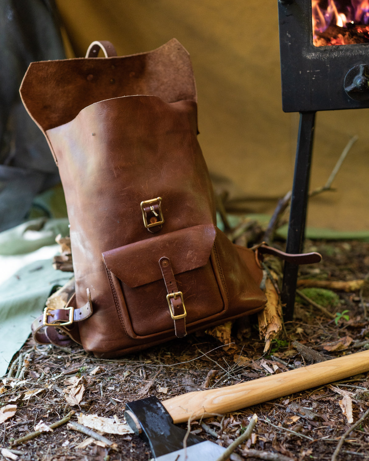 Brown leather backpack with bronze buckles in a camping tent, with an ax next to it.