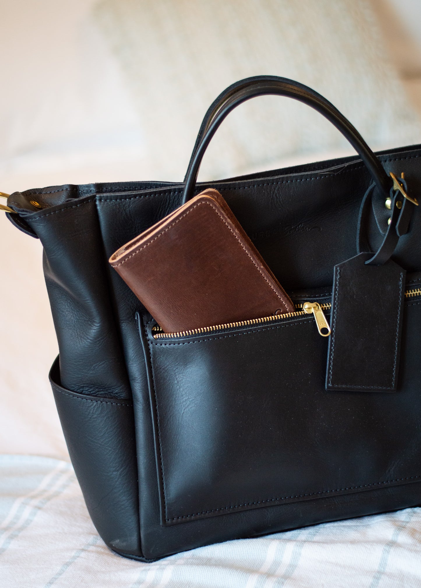brown leather passport wallet sticks out of the front pocket of a black legacy voyager tote. 