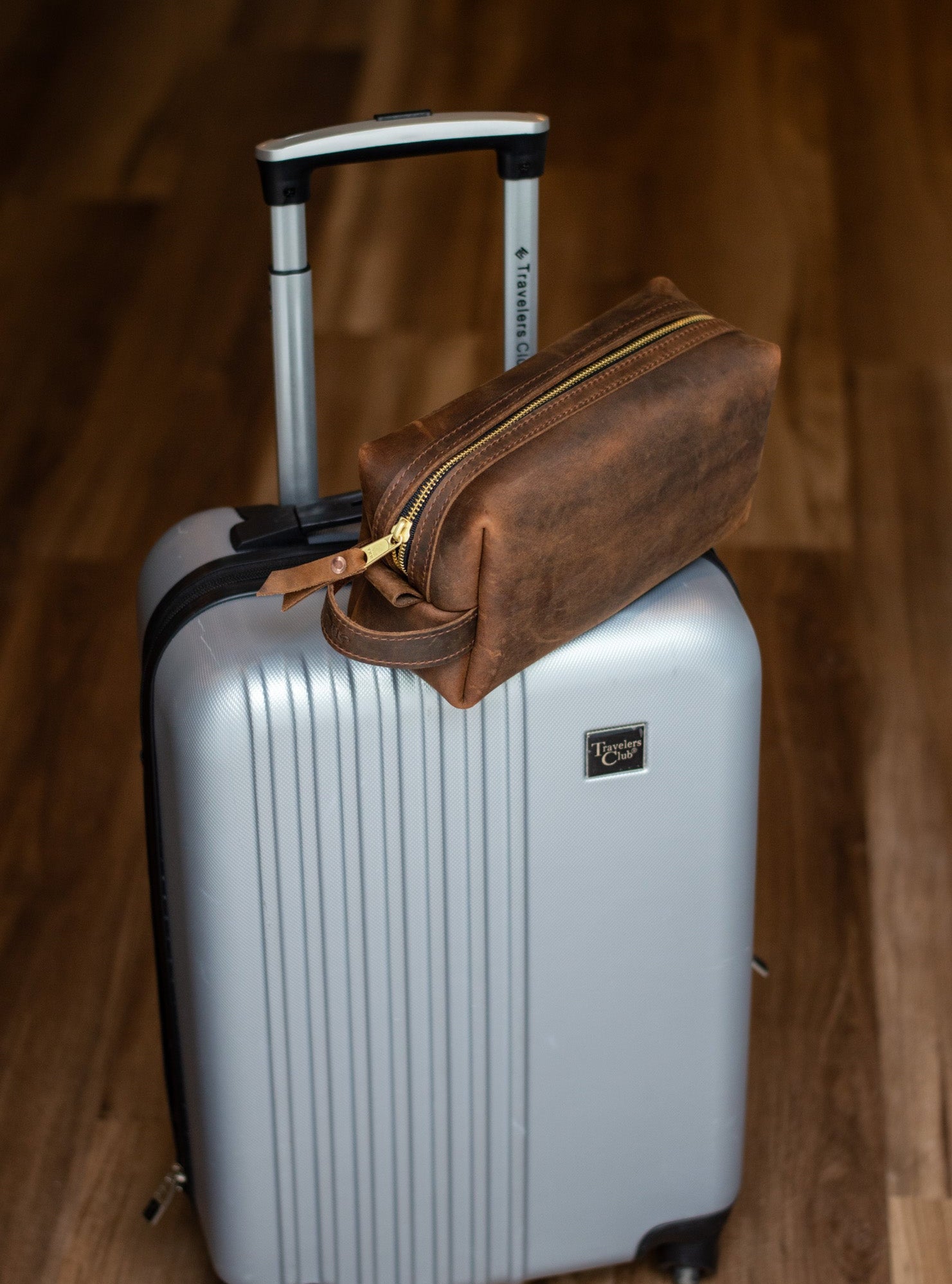 Silver suitcase with a brown leather toiletry bag sitting on top.