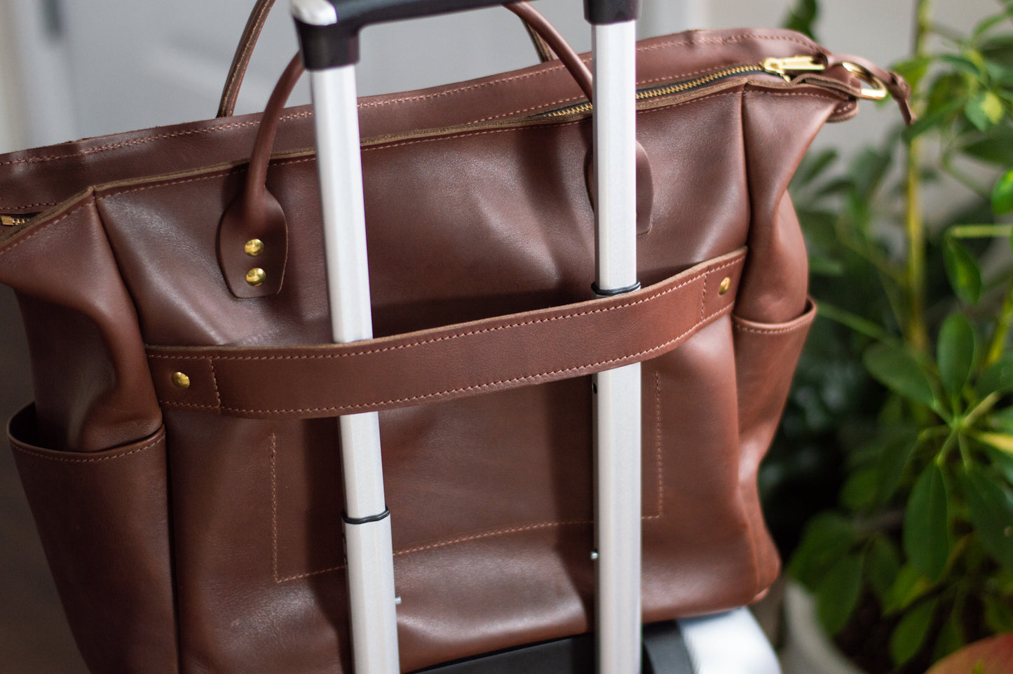 The Urban Southern Legacy Voyager bag is shown slipped over the handle of a travel suitcase. 