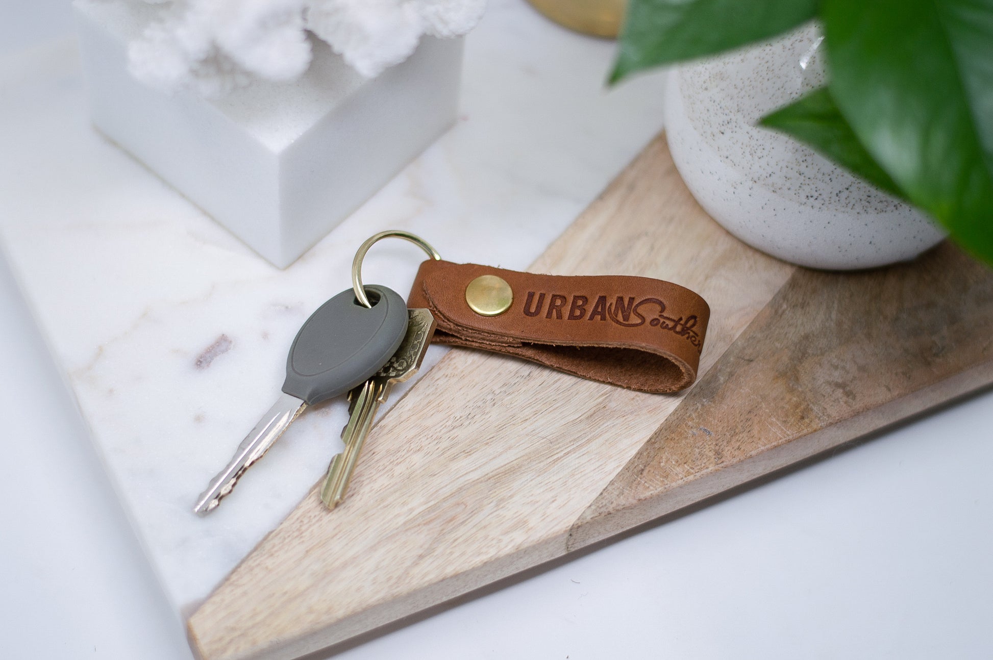 A set of keys attached to a honey Urban Key Fob, sit on an entryway table. 